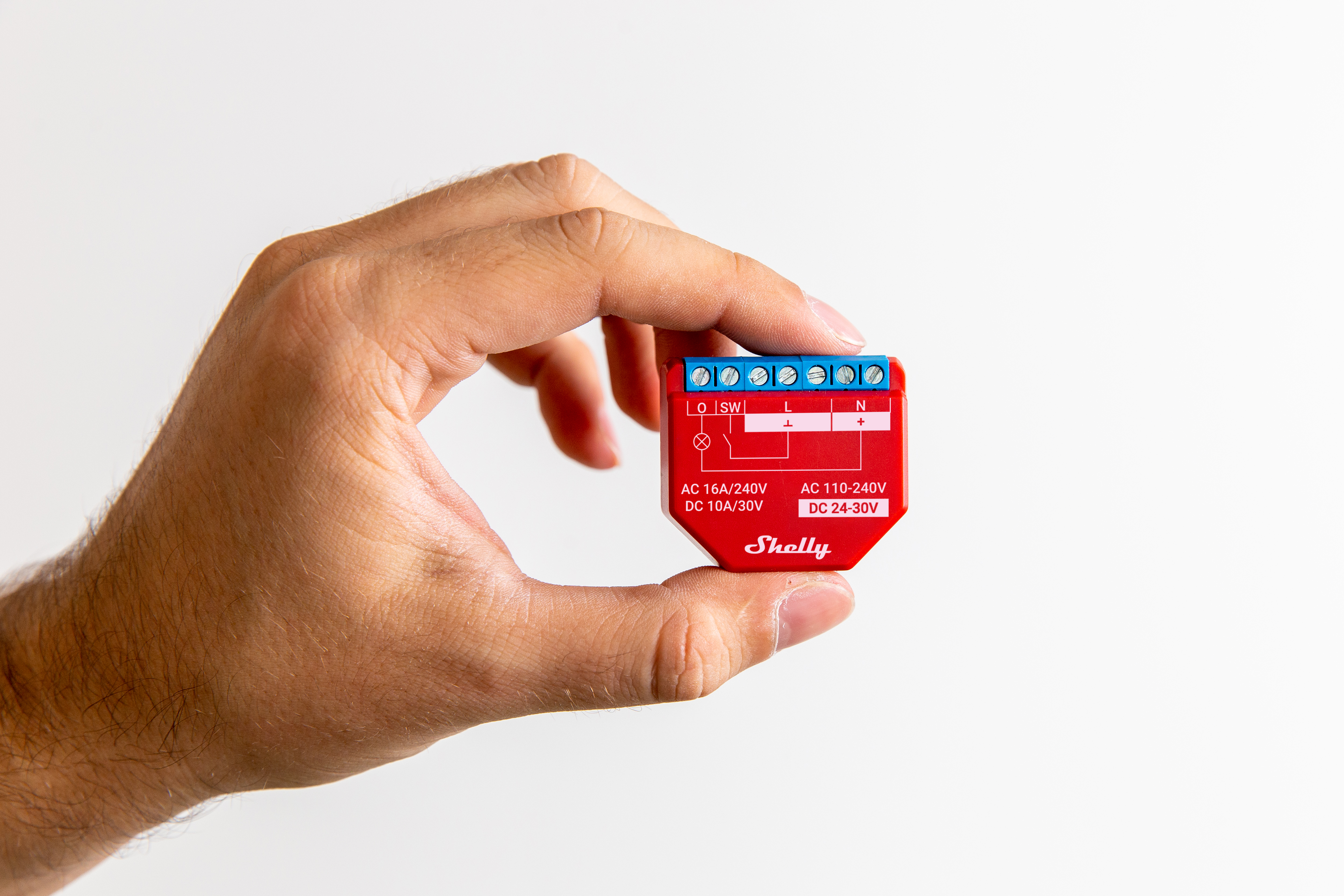 Una mano tiene un dispositivo Shelly rosso con terminali blu.