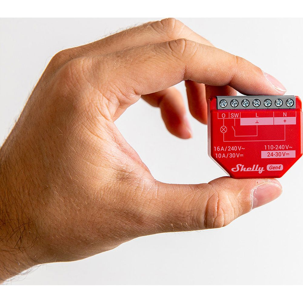 Una mano tiene un piccolo dispositivo rosso Shelly Gen4 con terminali ed etichette.
