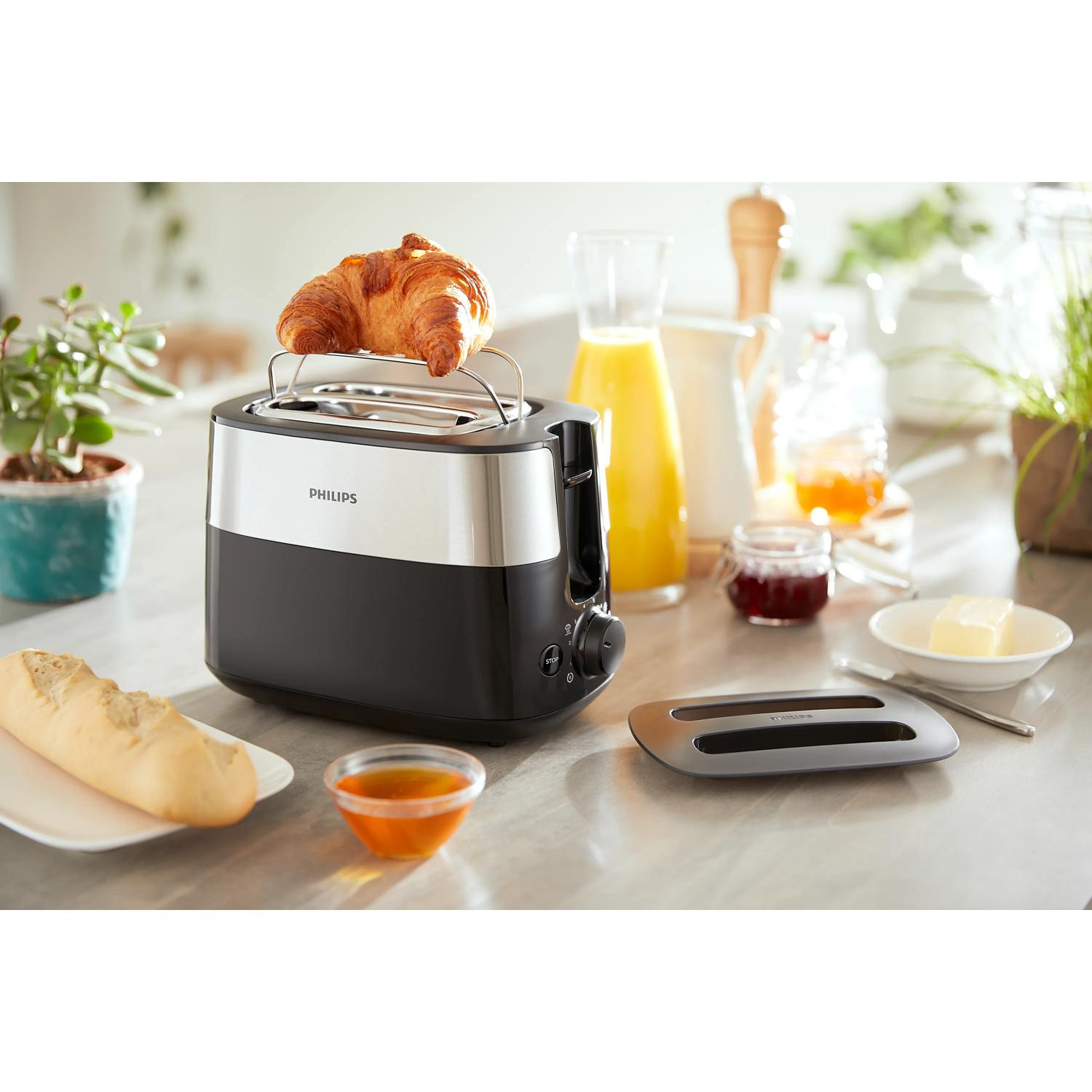 Ein Toaster mit einem Croissant, daneben Brot, Marmelade und Saft.