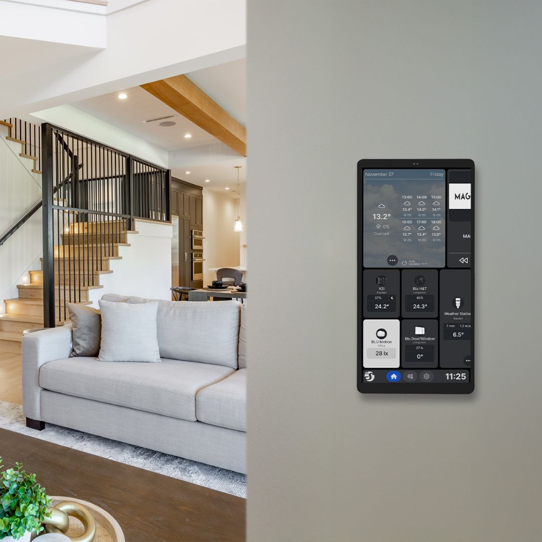 Soggiorno moderno con divano, scale e pannello smart home che mostra meteo e dati.