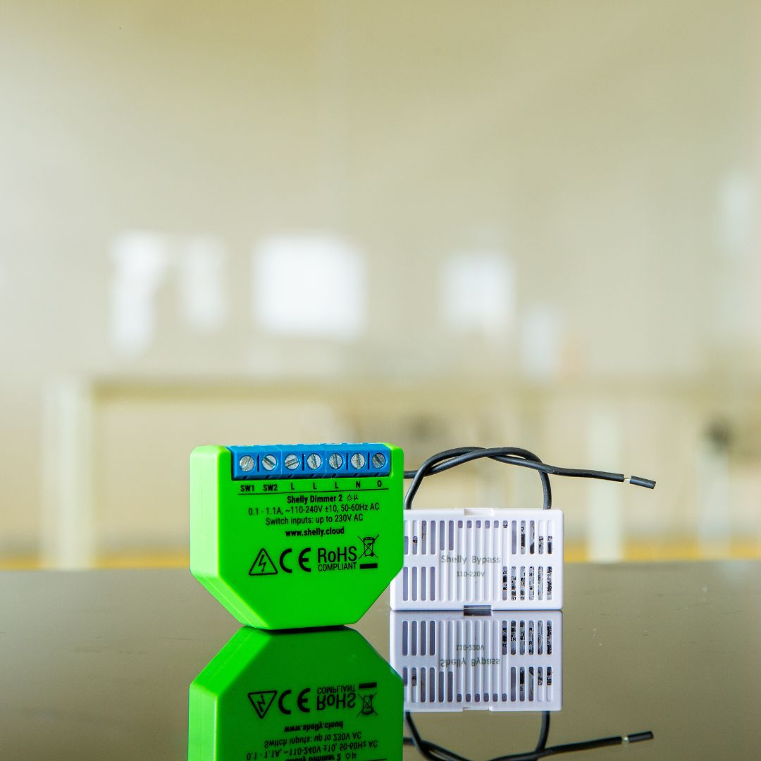 Un Shelly Dimmer 2 verde e un dispositivo Shelly Bypass bianco su un tavolo nero.