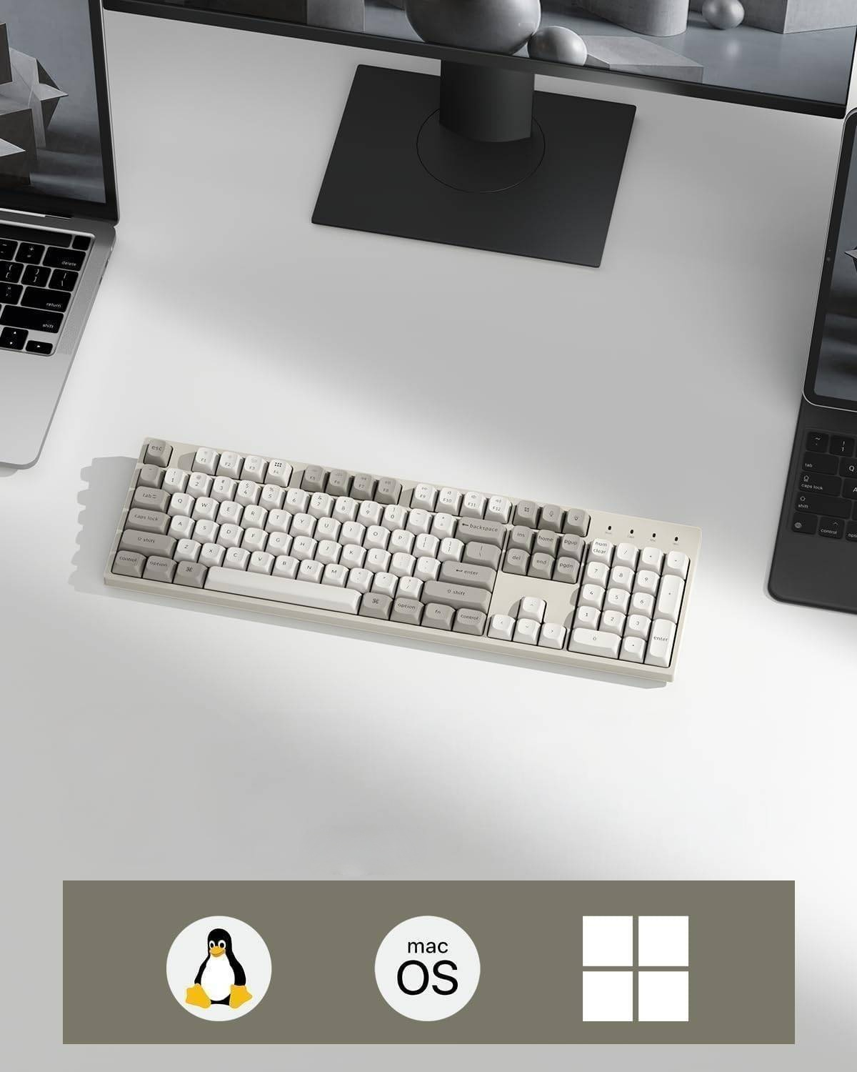 Biała klawiatura na biurku między laptopami a monitorem.