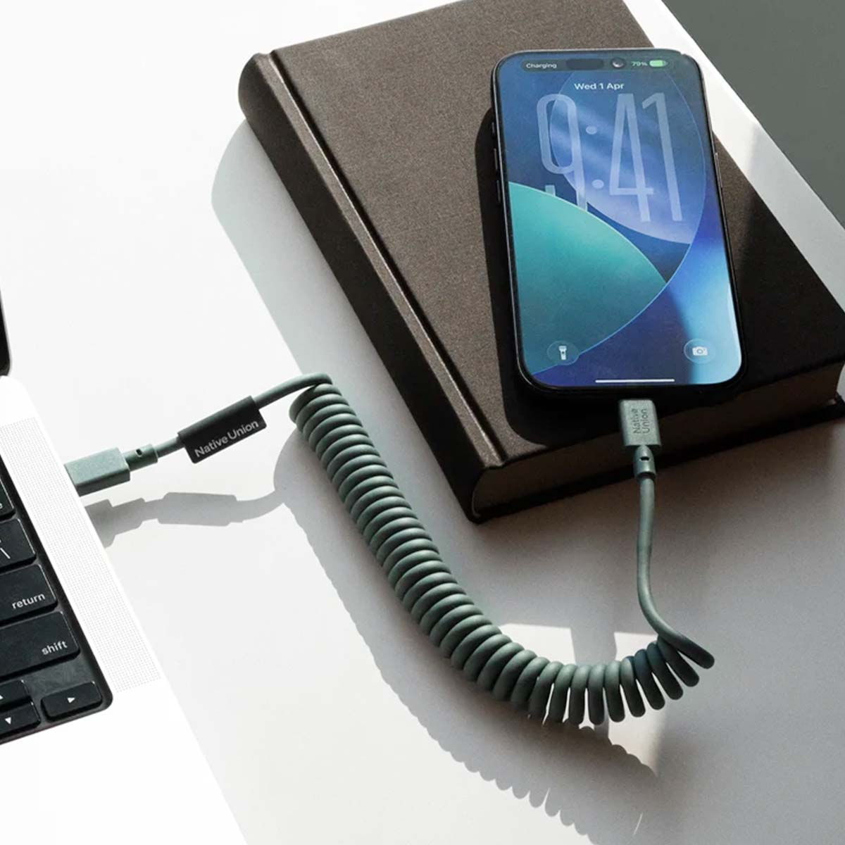 Un cavo di ricarica a spirale collega uno smartphone a un laptop su un tavolo.