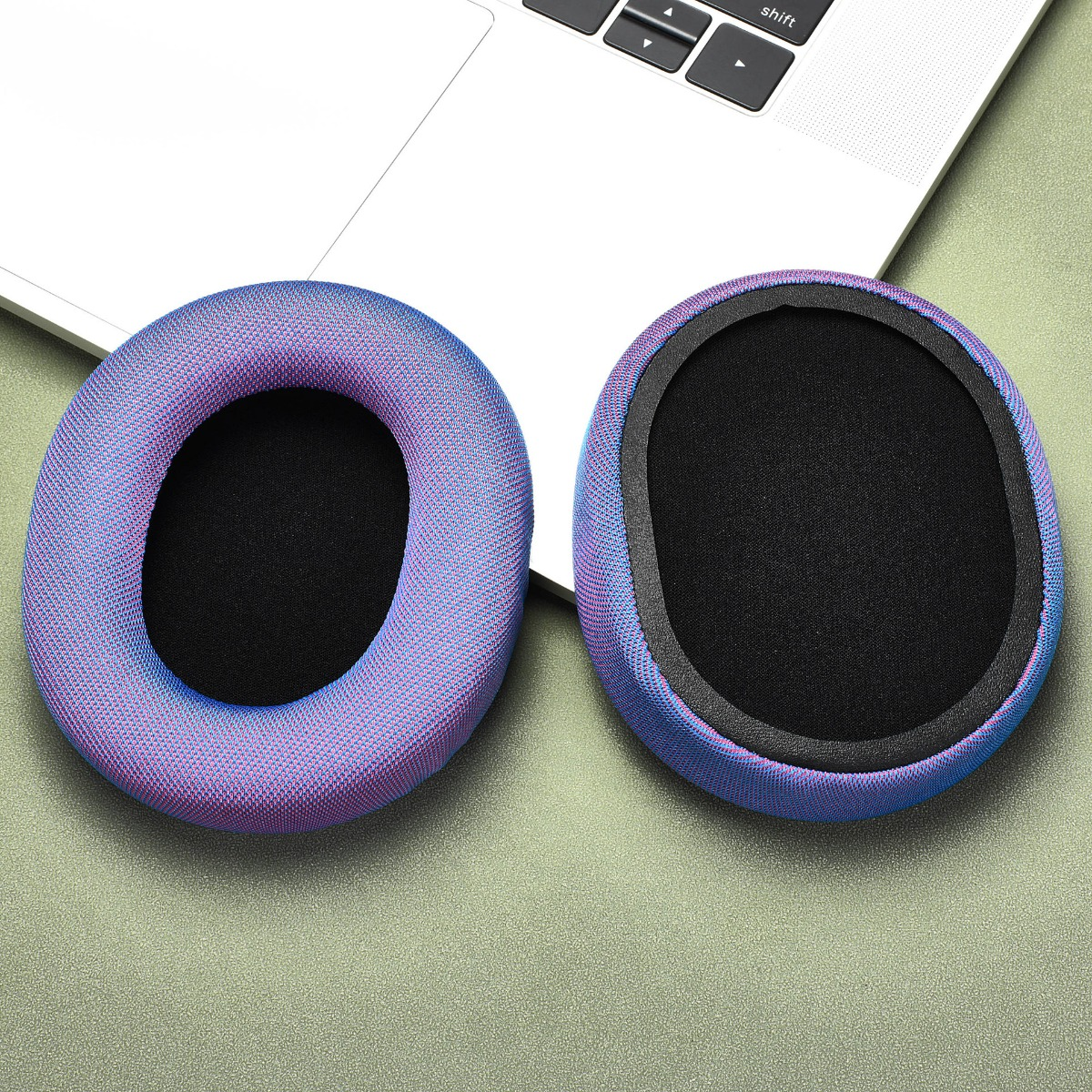Due cuscinetti per cuffie viola e blu sono uno accanto all'altro su una superficie verde vicino a un laptop.