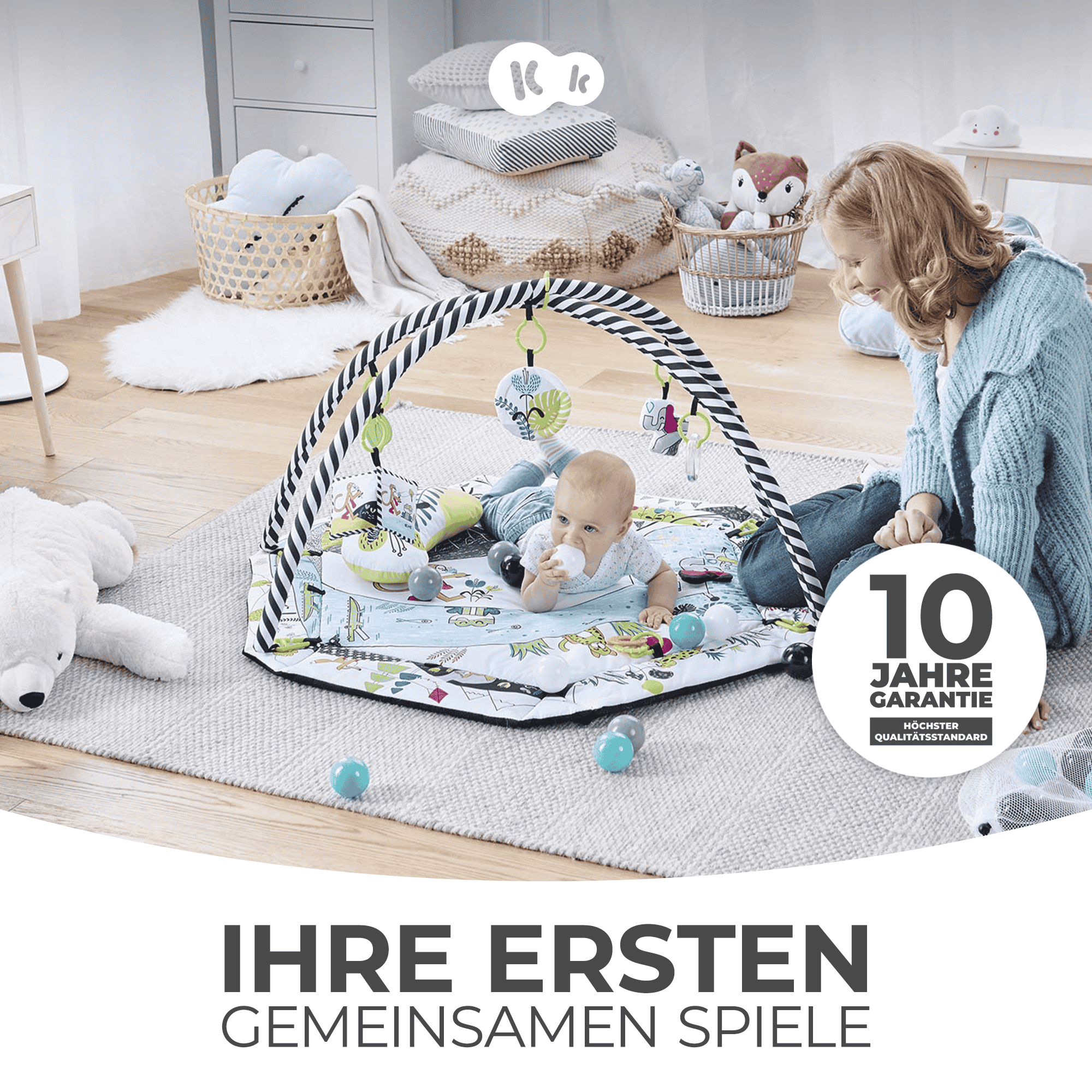 Eine Frau und ein Baby spielen auf einer Spielmatte mit bunten Spielzeugen und einem Bären.