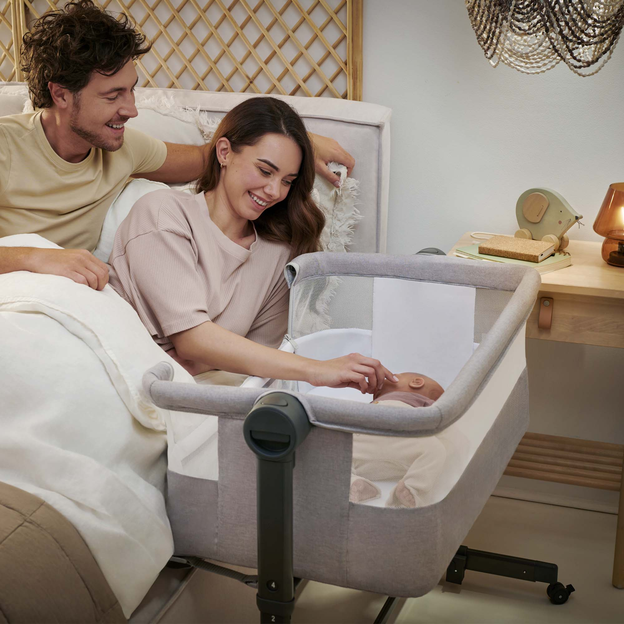 Ein glückliches Paar blickt auf ihr Baby in einem Beistellbett neben ihrem Bett.