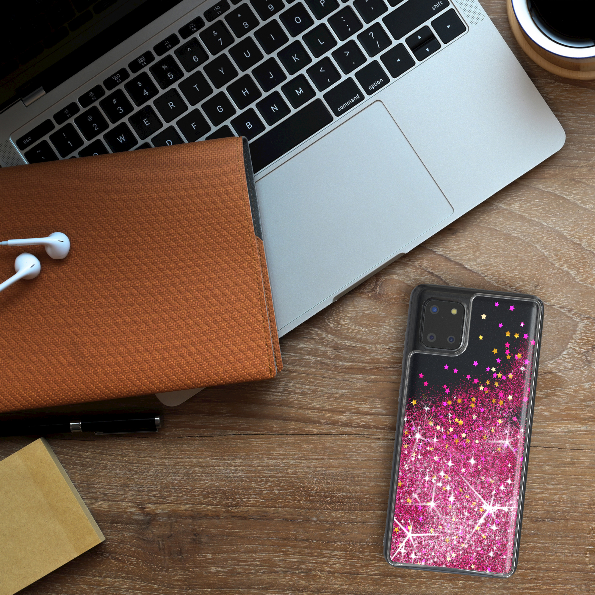 Laptop, Notizbuch, Kopfhörer, Stift und Handy mit pinken Glitzersternen auf Holzschreibtisch.