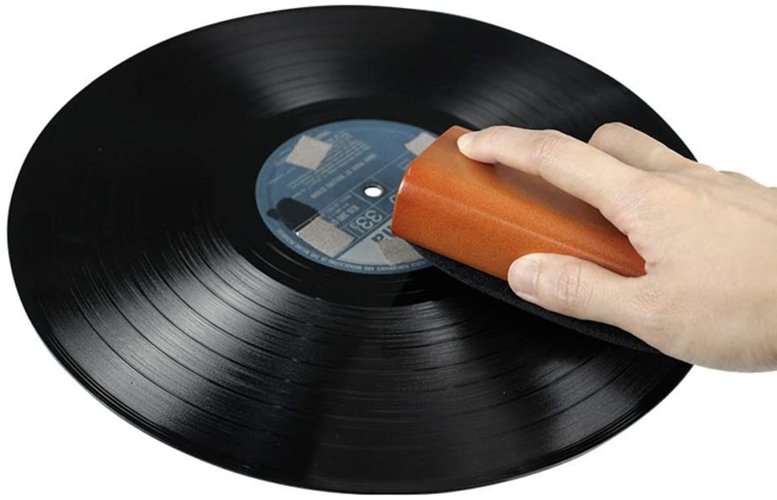 Dłoń czyści czarną płytę winylową brązowym narzędziem.