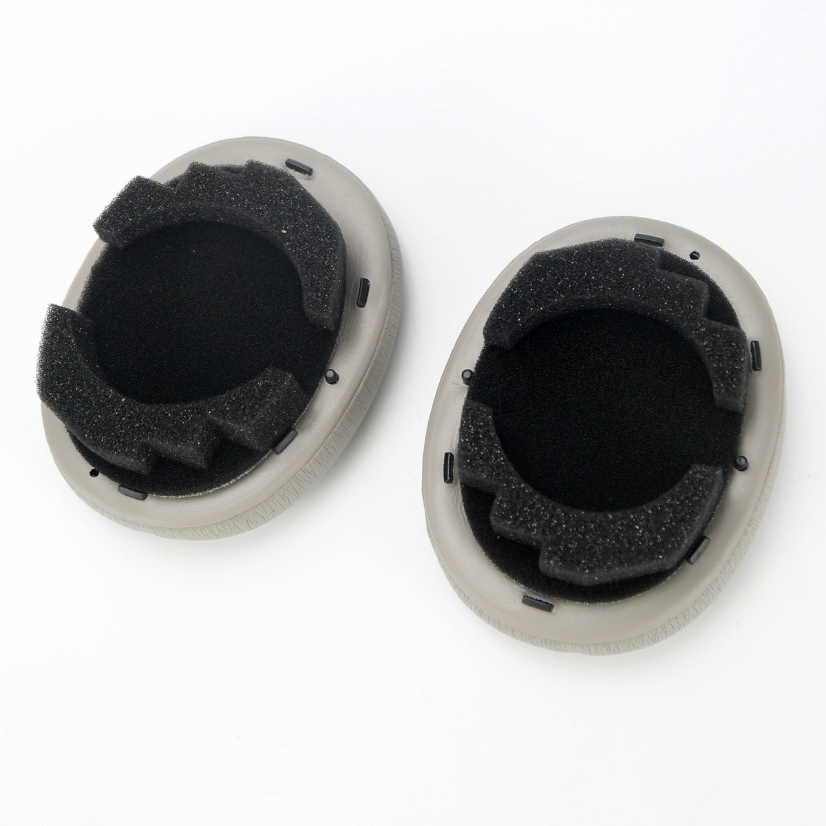 Dos almohadillas grises para auriculares con inserciones de espuma negra, sobre fondo blanco.