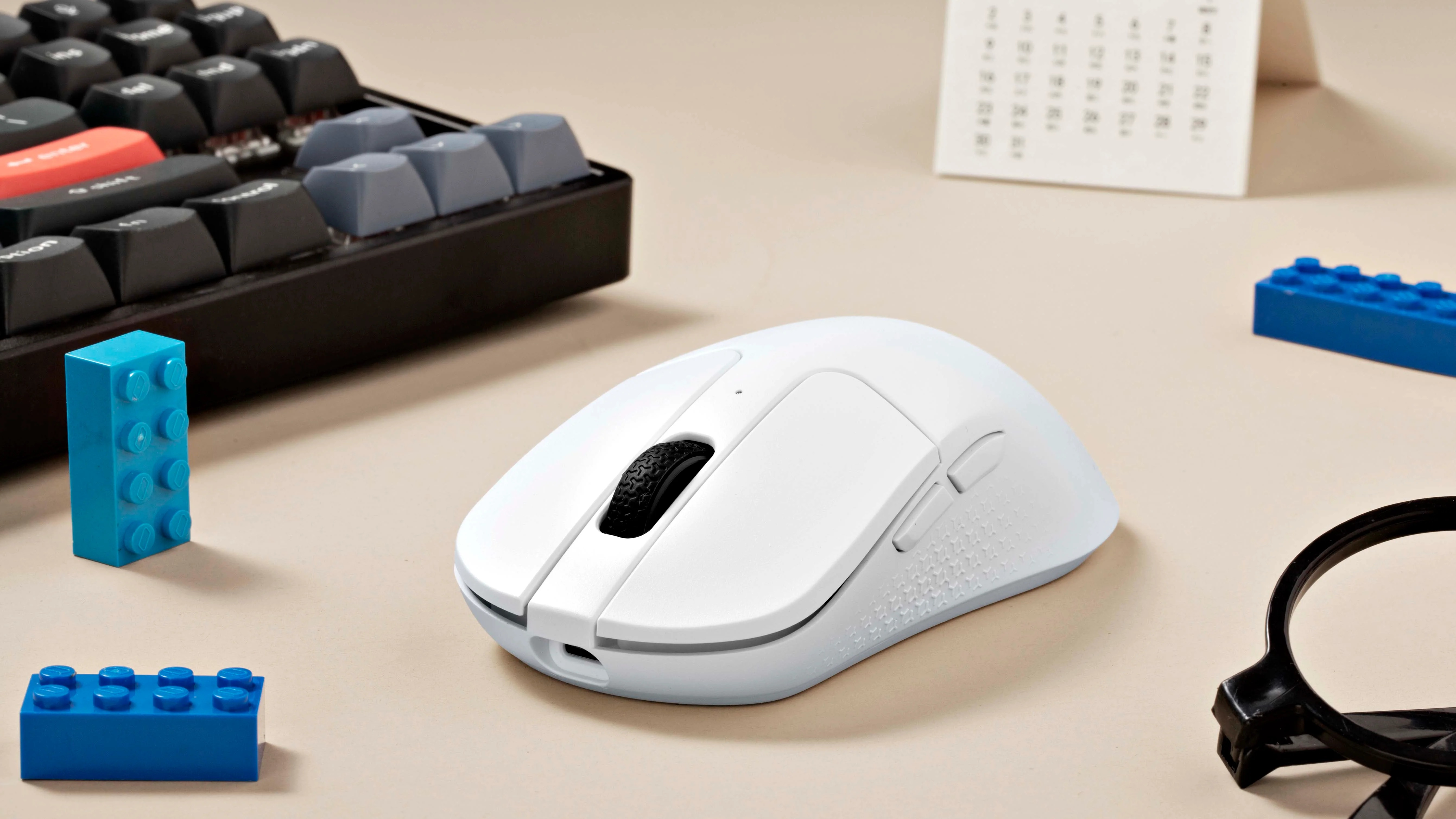 Biała mysz leży obok klawiatury i niebieskich klocków Lego.