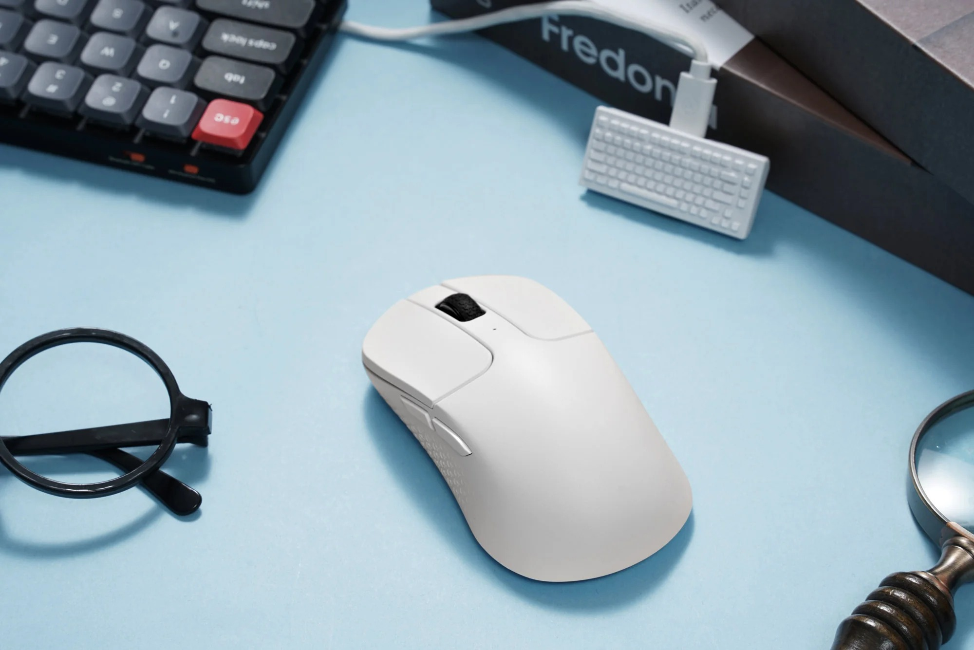 Biała mysz, klawiatura, okulary i lupa na niebieskim tle.