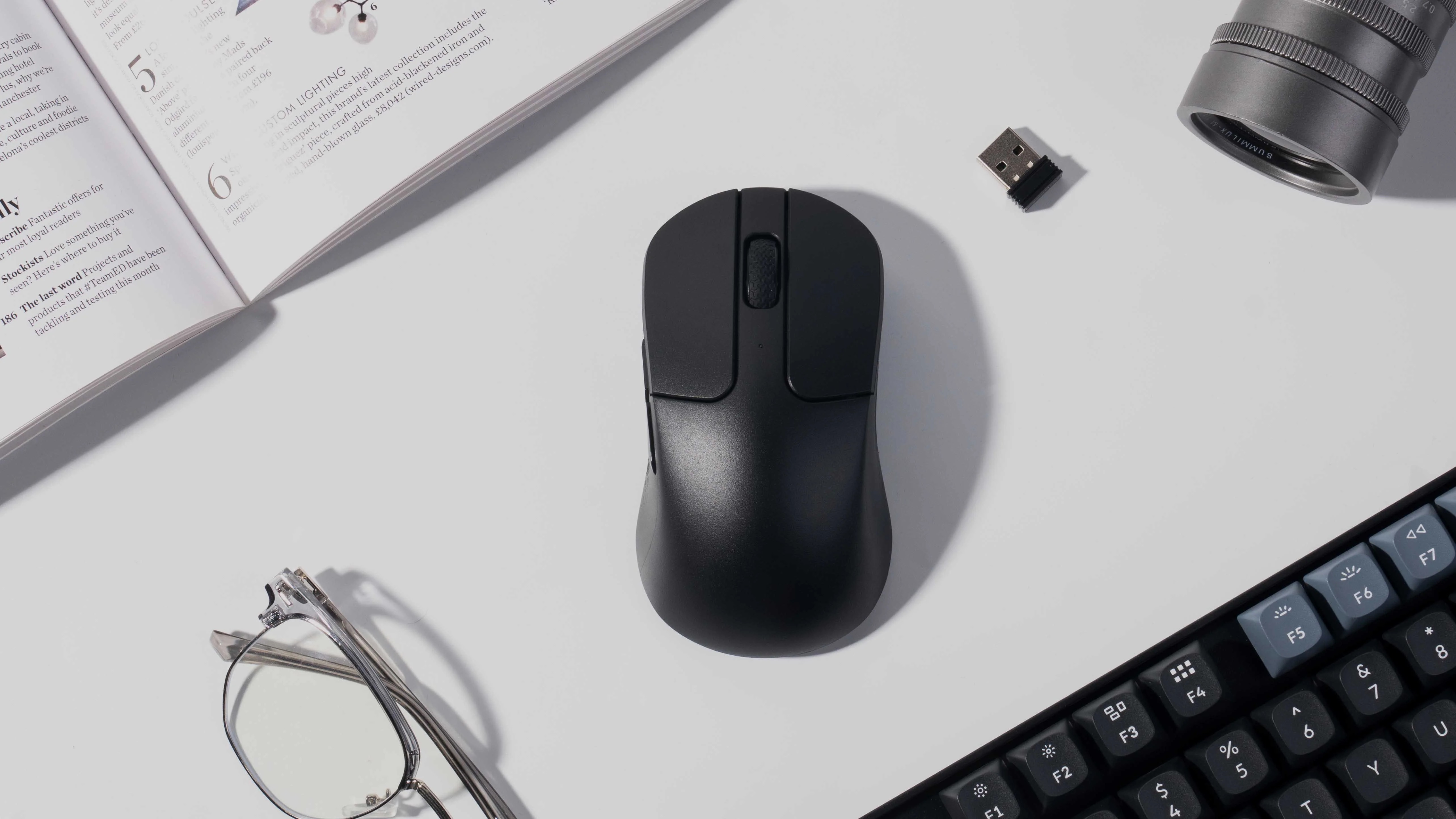 Czarna mysz, klucz USB, klawiatura, okulary i obiektyw aparatu na białej powierzchni.