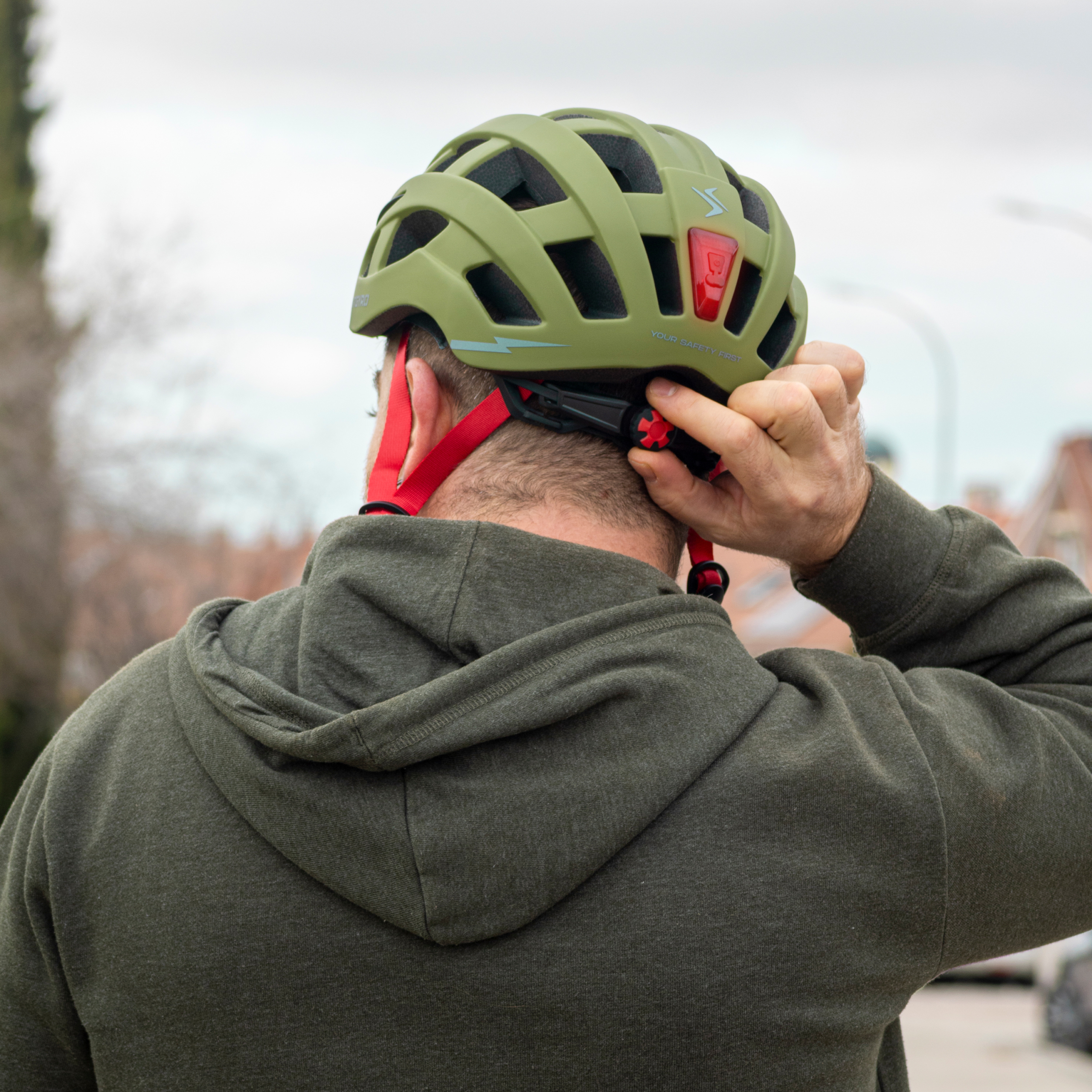 Hombre ajusta casco verde oliva con correa roja y luz.