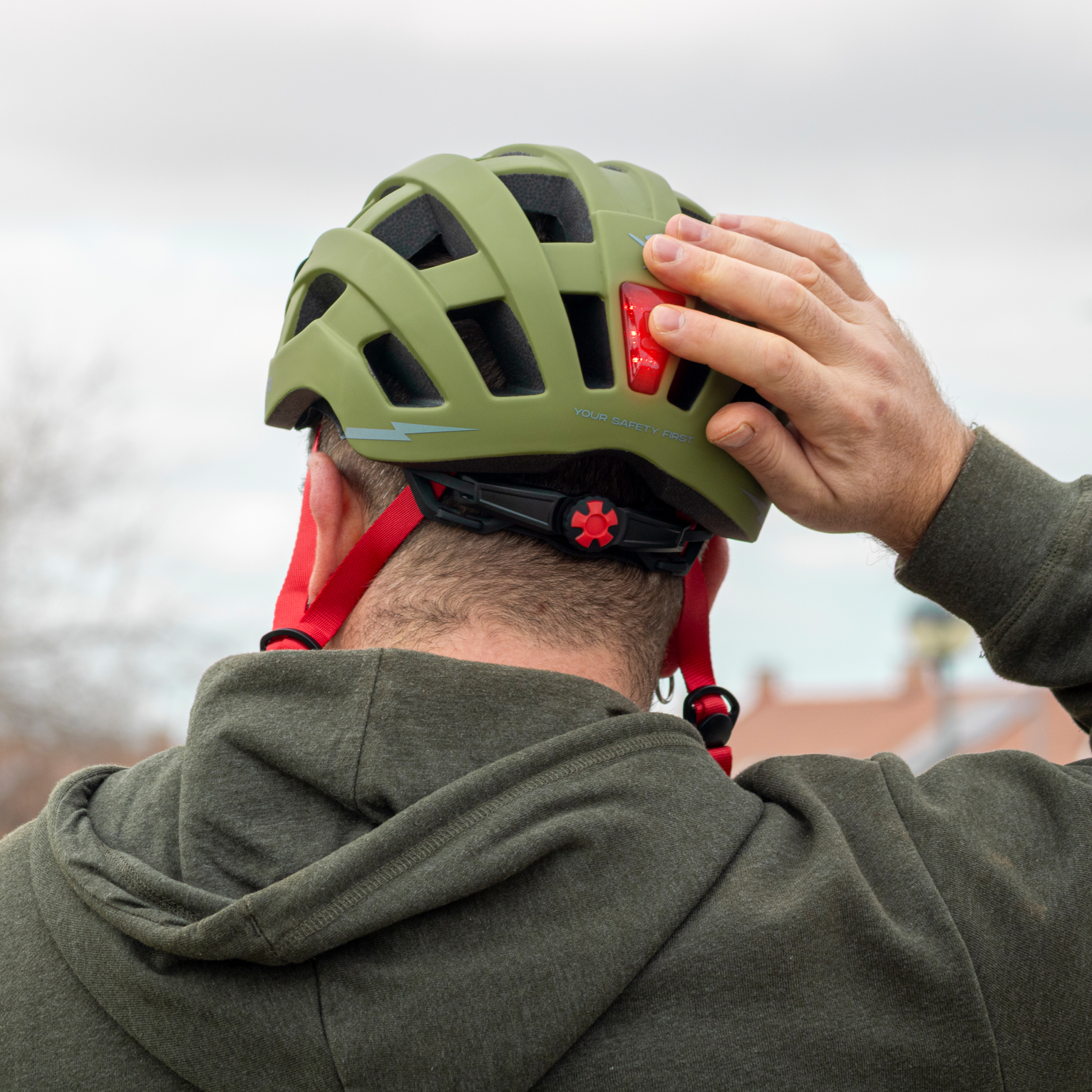 Un hombre con casco verde y correa roja presiona la luz trasera.