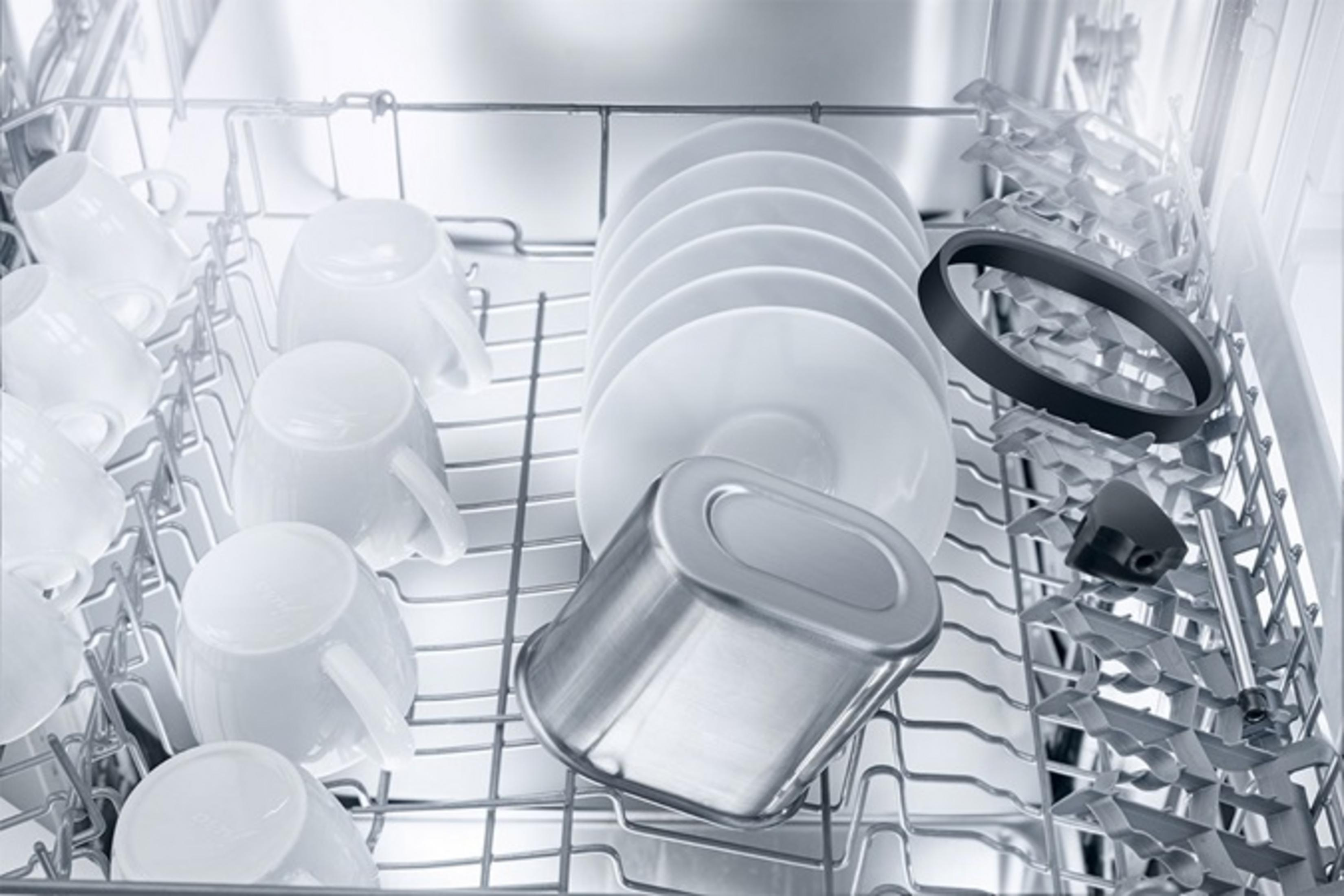 Tazas blancas, platos y un recipiente de metal en un lavavajillas.