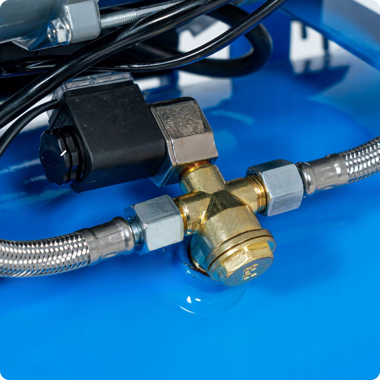 Złoty zawór z elastycznymi wężami i przewodami, zamontowany na niebieskim zbiorniku.