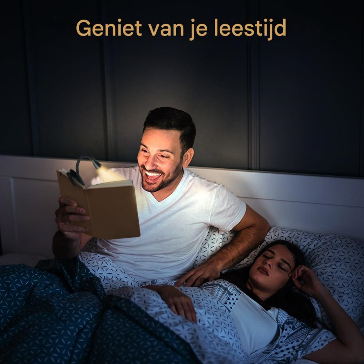 Ein Mann liest im Bett bei Nacht mit einer Buchlampe, während eine Frau neben ihm schläft.
