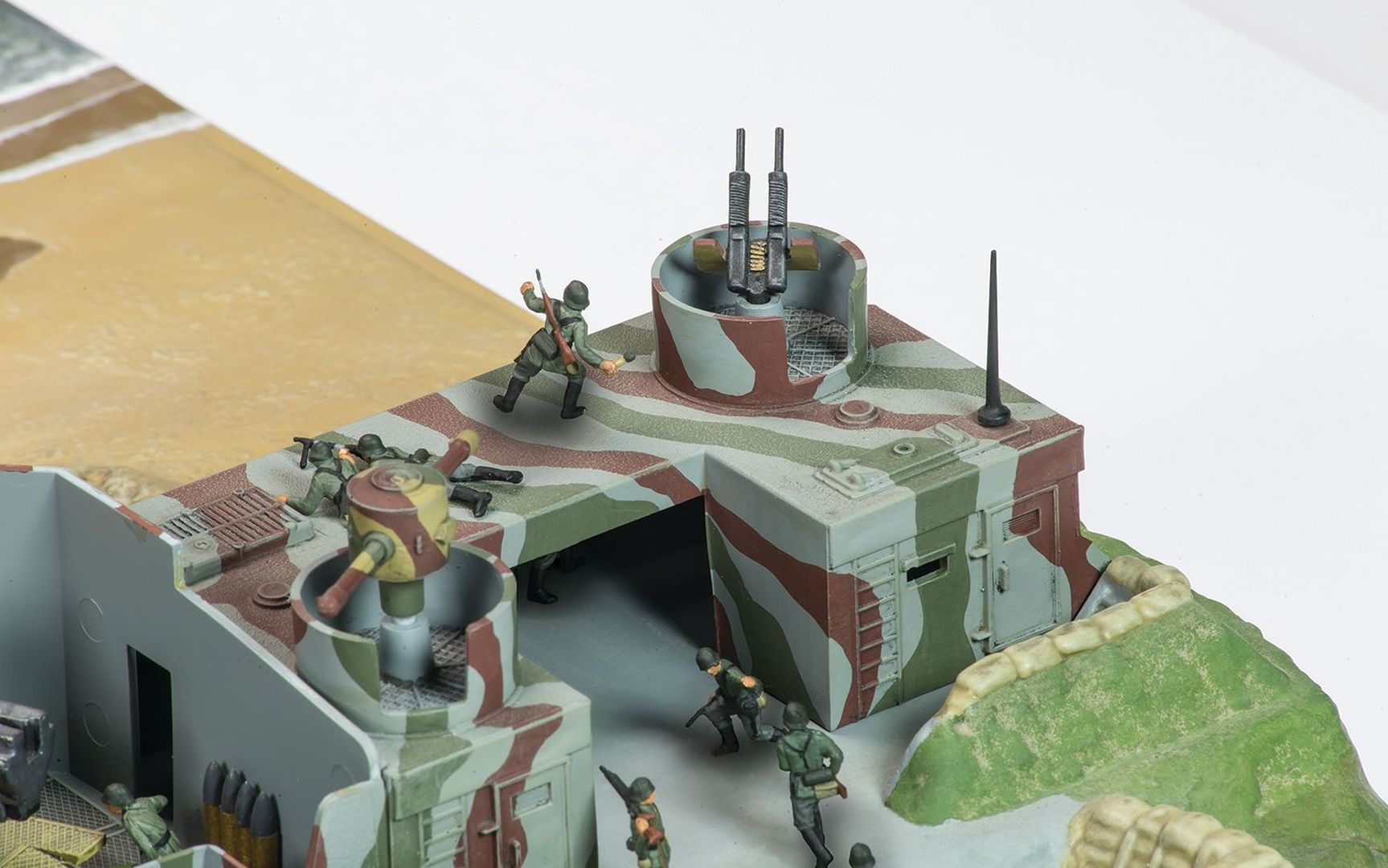 Miniaturowa forteca z żołnierzami i działami w kamuflażu, na plaży.