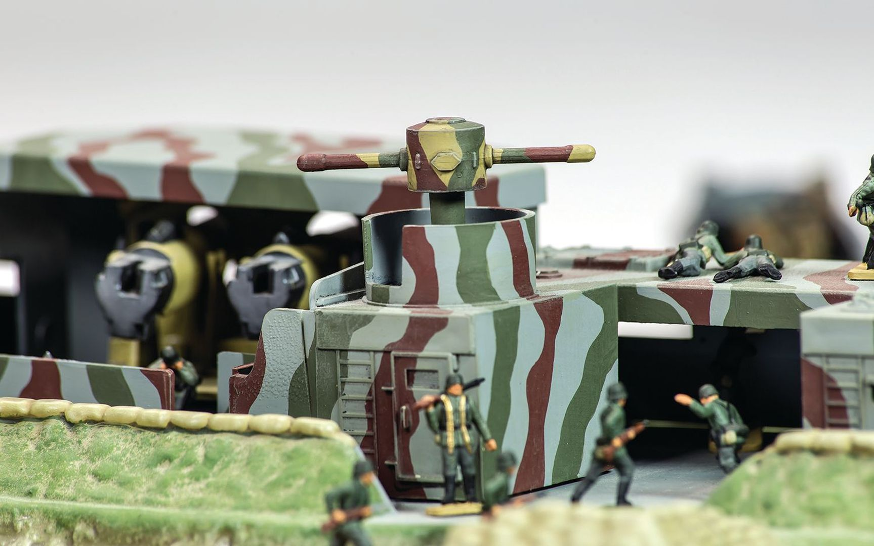 Czołg modelarski z kamuflażem, żołnierze w zielonych mundurach, niektórzy leżą.