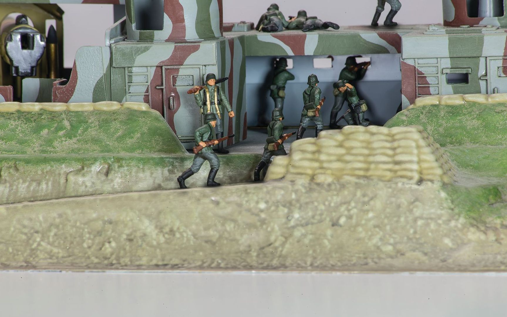 Miniaturowi żołnierze w mundurach maskujących maszerują na polu bitwy z workami z piaskiem.
