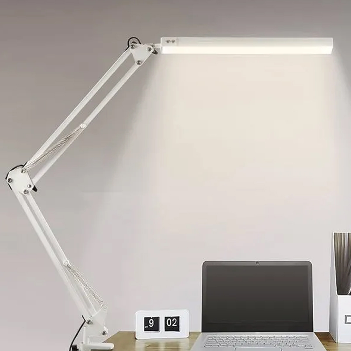 Eine weiße Schreibtischlampe über einem Laptop mit einem Flipclock daneben.