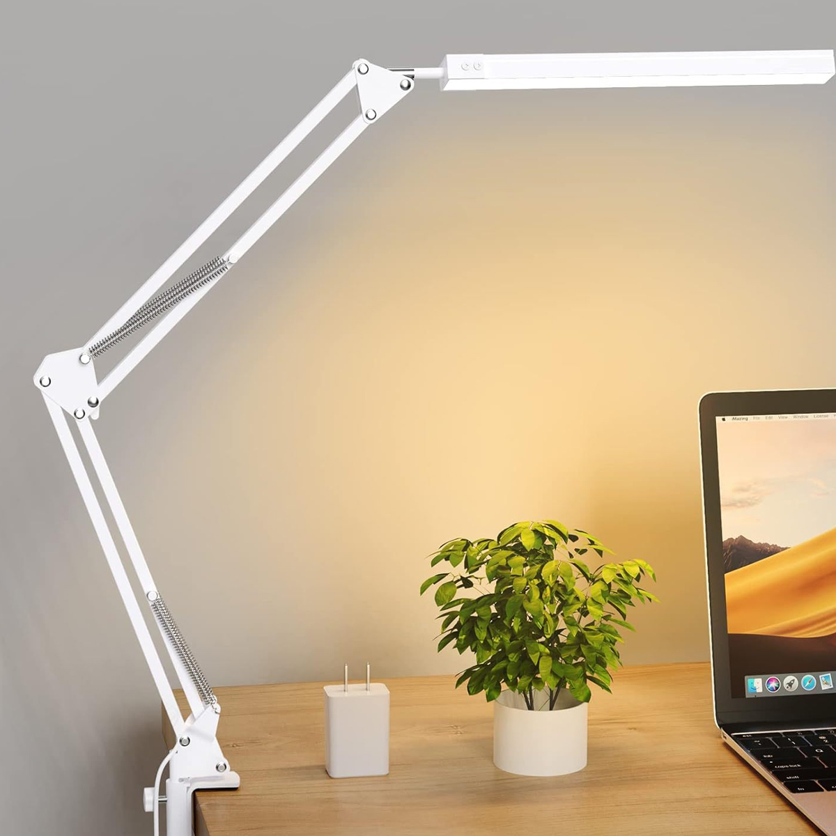 Eine weiße, verstellbare LED-Schreibtischlampe steht auf einem Holztisch neben einem Laptop, einer Pflanze und einem Ladegerät.