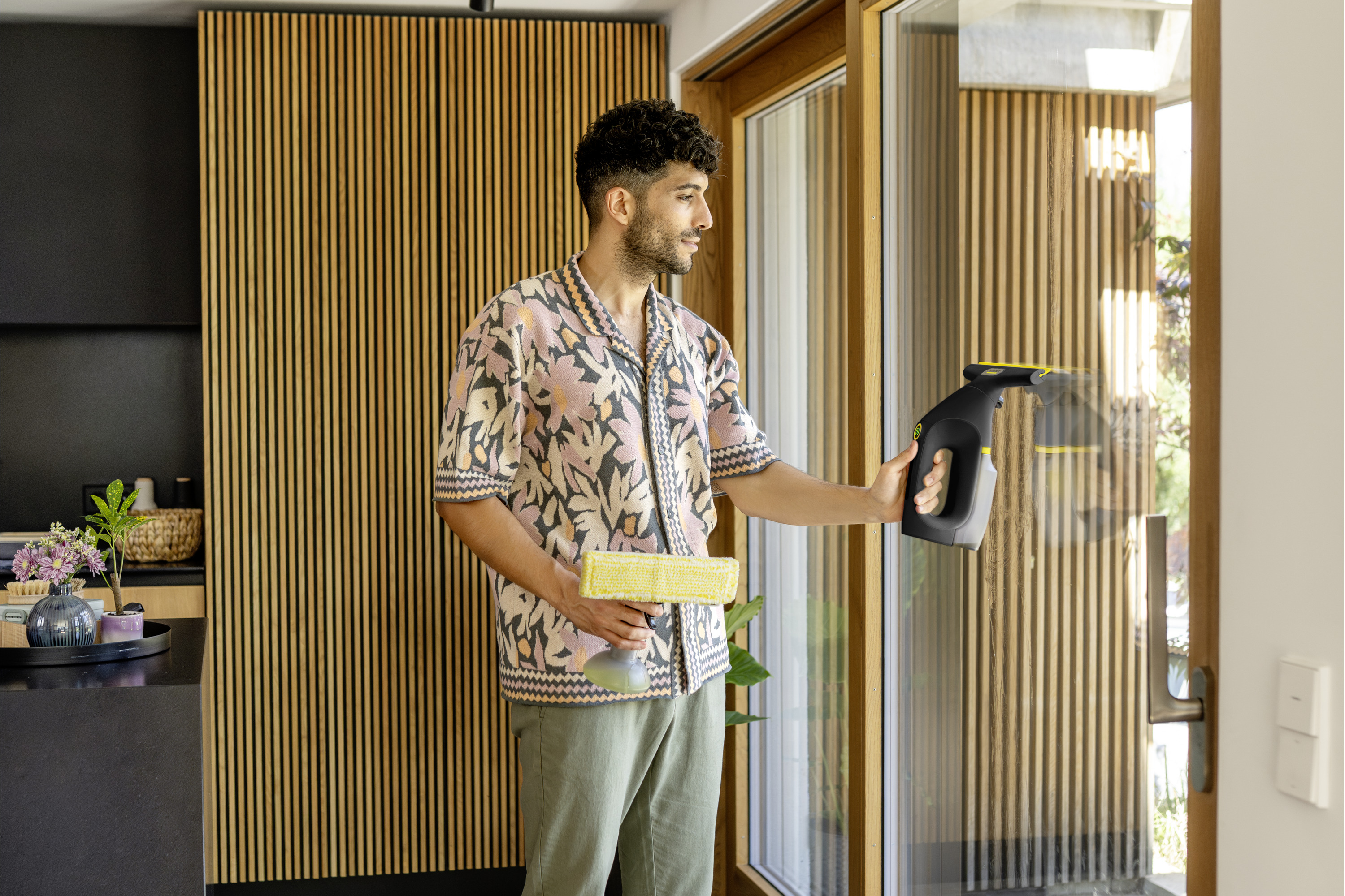 Mann reinigt Fenster mit einem Akku-Fenstersauger und einem gelben Tuch.
