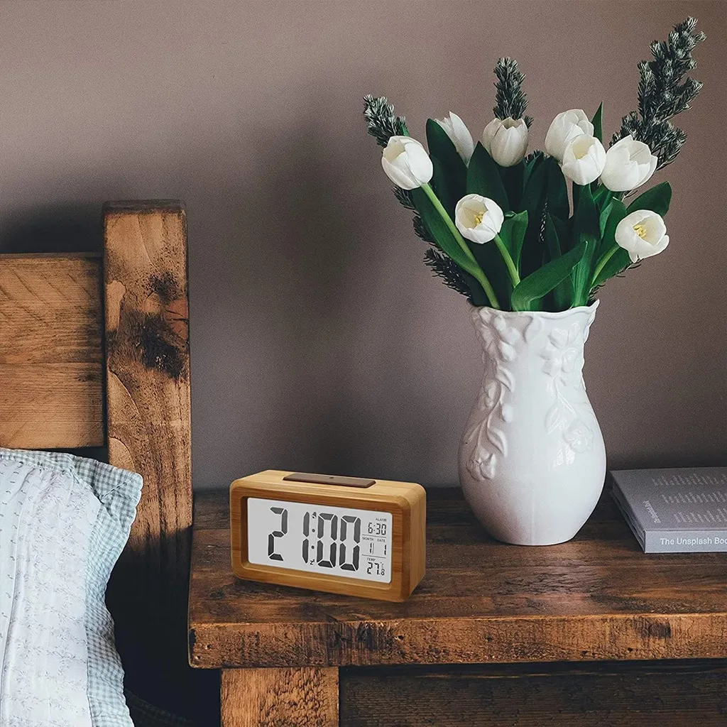 Holzwecker auf Nachttisch mit weißen Tulpen in einer Vase.