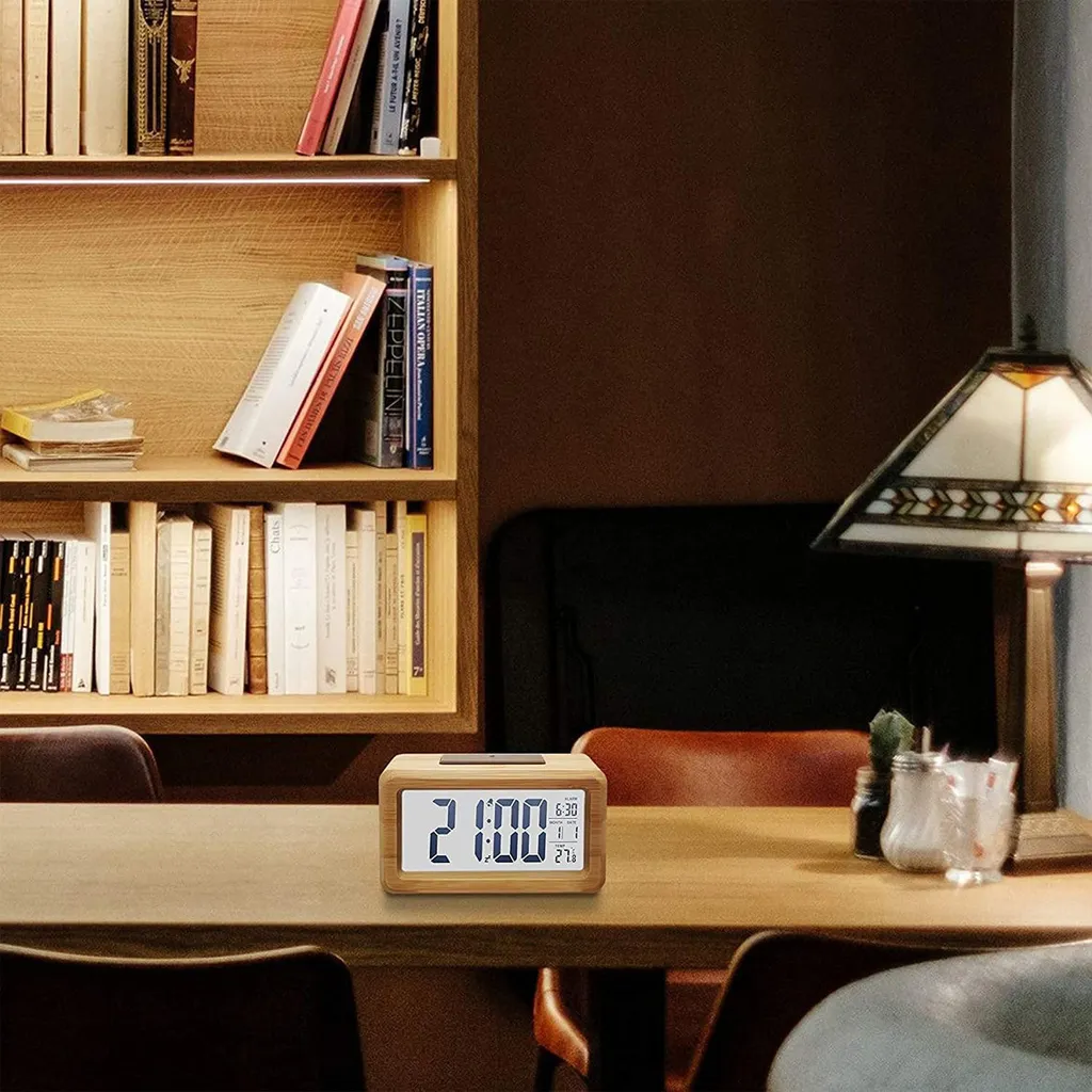 Ein hölzerner Digitalwecker zeigt 21:00 auf einem Tisch vor einem Bücherregal.