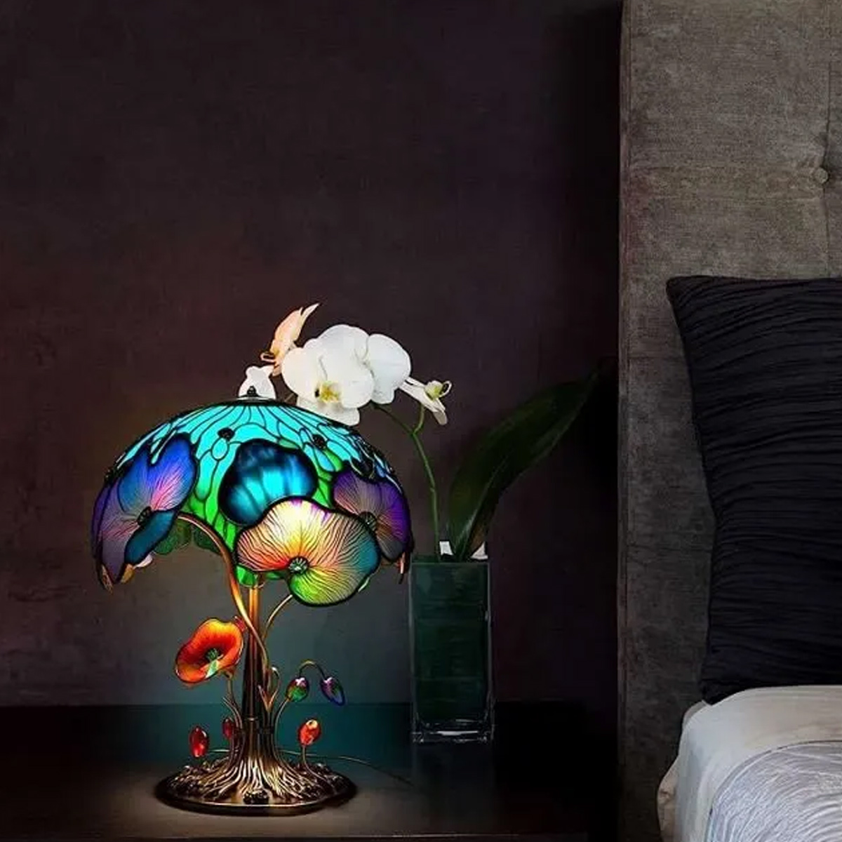 Bunte Tiffany-Lampe mit Blumenmuster, neben einem Bett mit Orchideen.