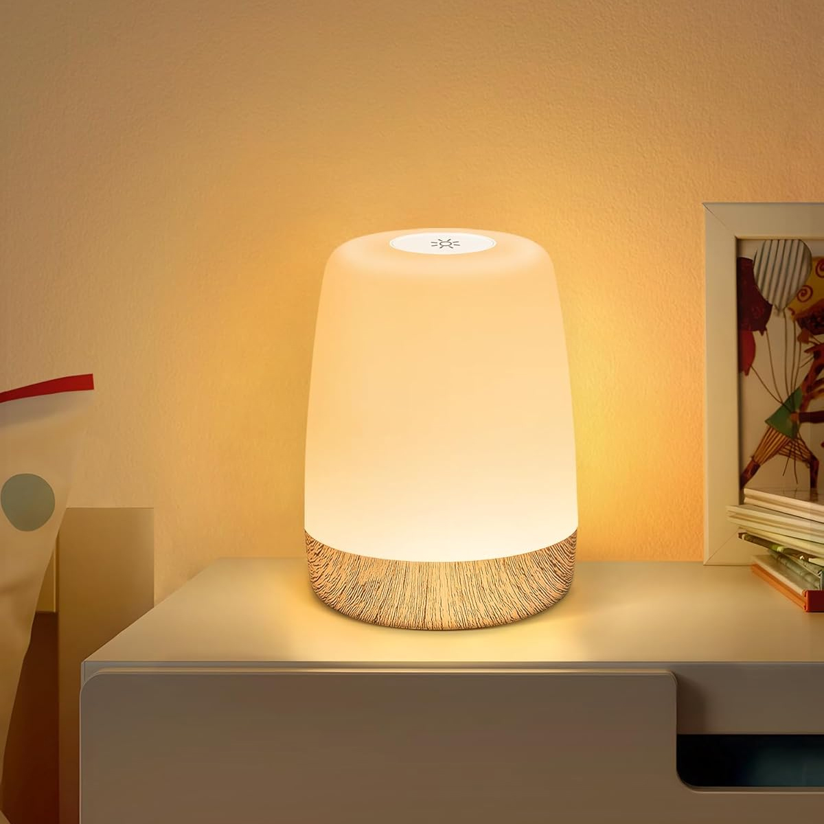 Eine leuchtende weiße Lampe mit Holzmaserungsbasis steht auf einem Nachttisch.