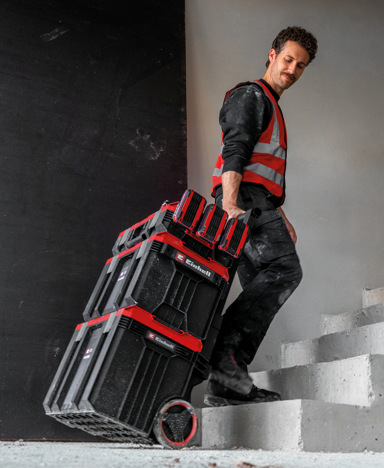 Mann in Warnweste zieht Werkzeugkasten die Treppe hoch.