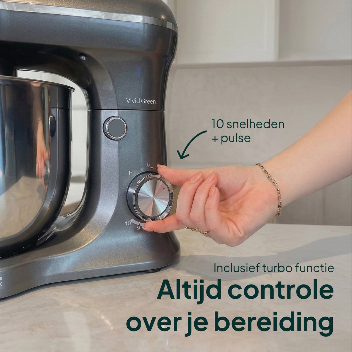 Gray stand mixer with stainless steel bowl. A hand turns the speed dial.