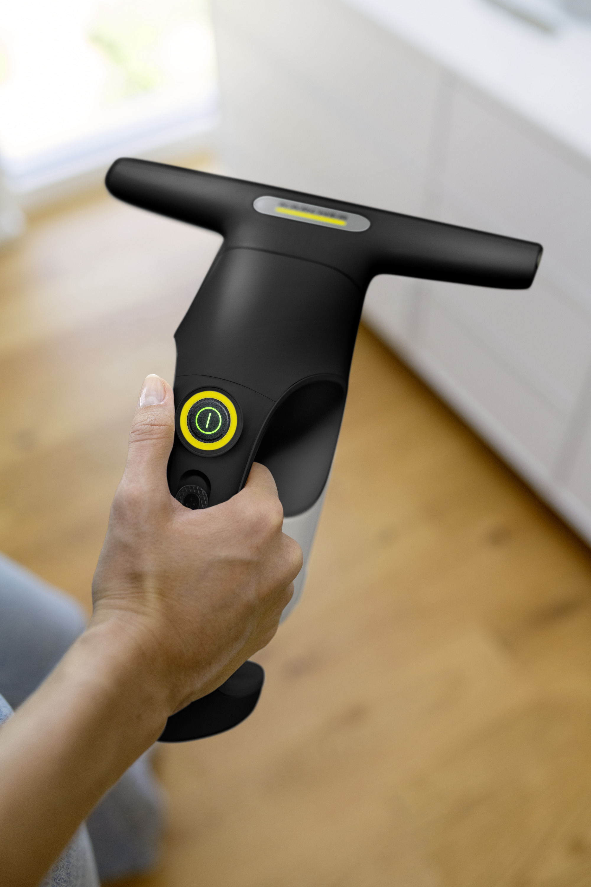 Eine Hand hält einen schwarzen Fensterreiniger mit einem grünen Ein-/Ausschaltknopf.