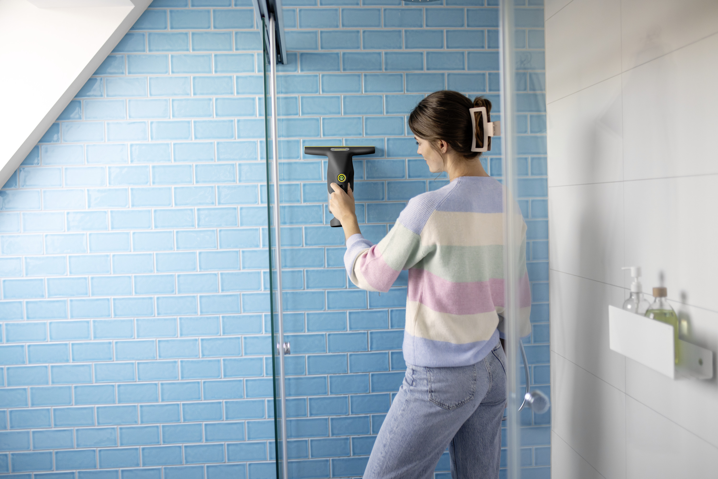 Eine Frau reinigt eine blaue Kachelwand mit einem Fensterreiniger.