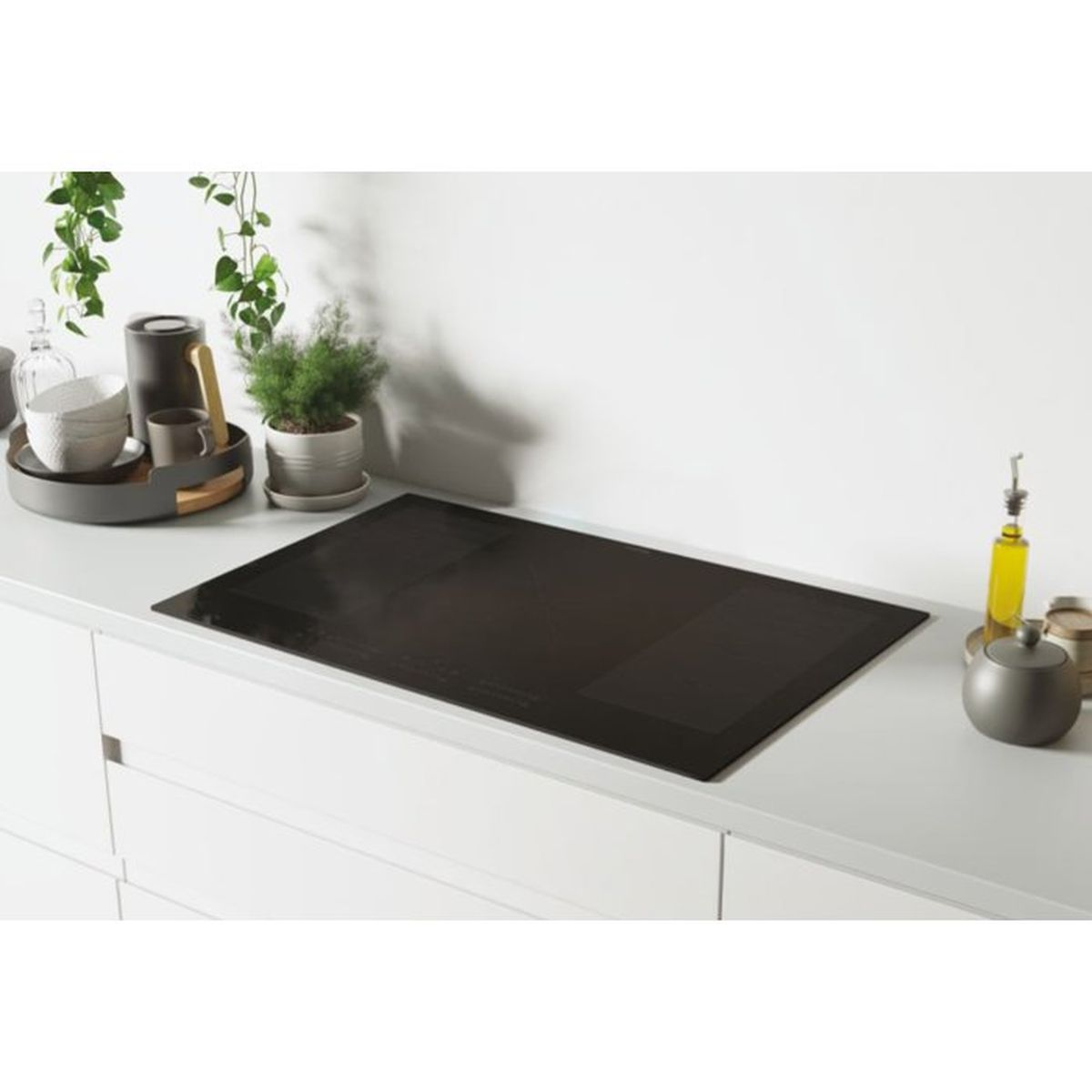Un piano cottura a induzione nero su un piano di lavoro bianco con oggetti decorativi.