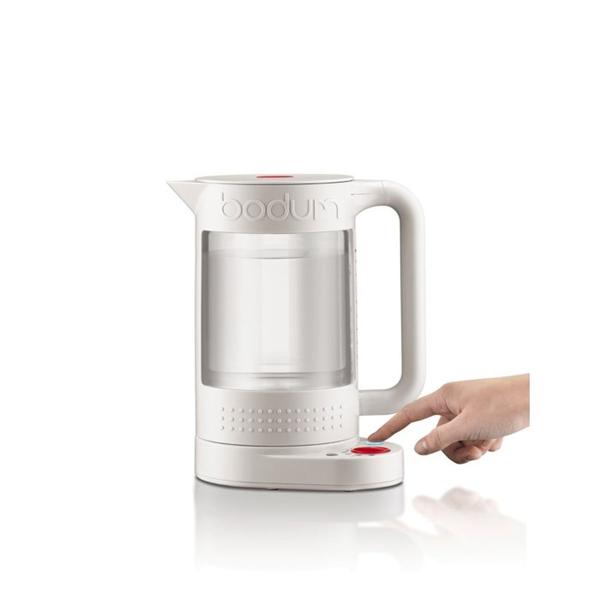Una tetera eléctrica blanca con cuerpo de vidrio y logo Bodum, un dedo pulsa el botón rojo.