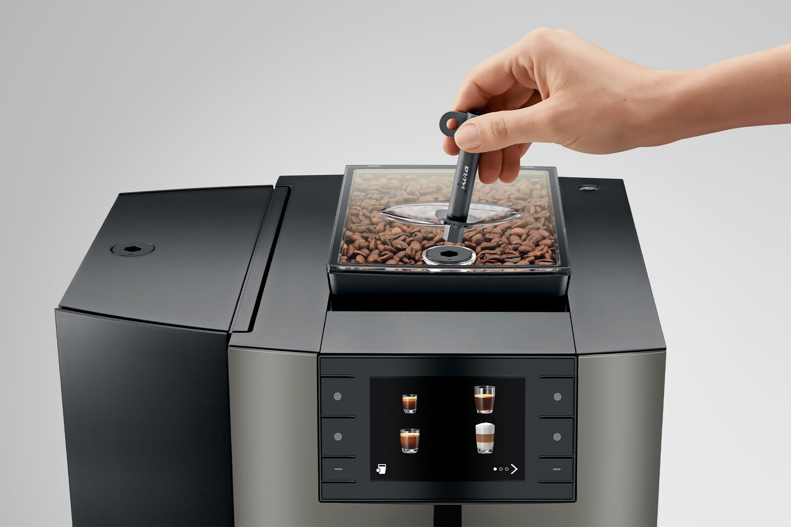 Una mano tiene un misurino sopra un contenitore di chicchi di caffè su una macchina da caffè.