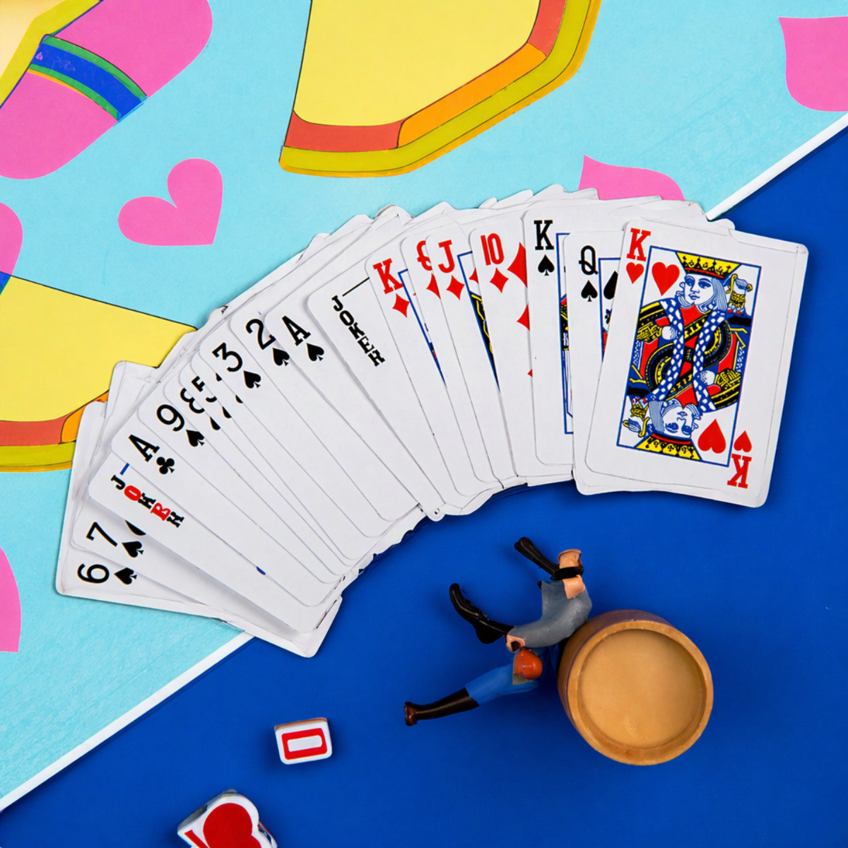 Een waaier speelkaarten, inclusief Jokers en Koningen, ligt op blauw oppervlak bij speelgoedfiguur.