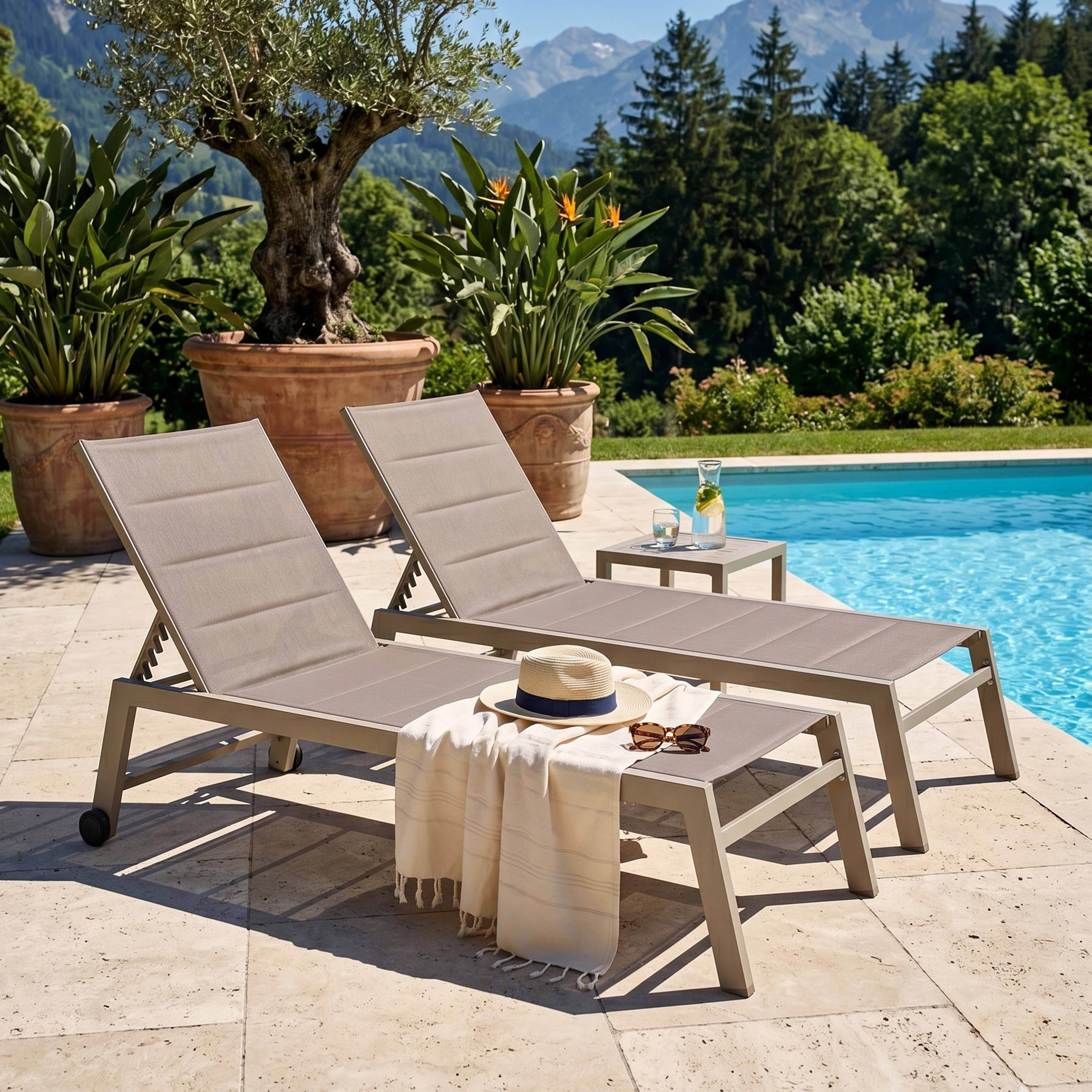 Zwei Liegestühle am Pool mit Bergkulisse. Ein Hut und Sonnenbrille liegen auf einem Handtuch.