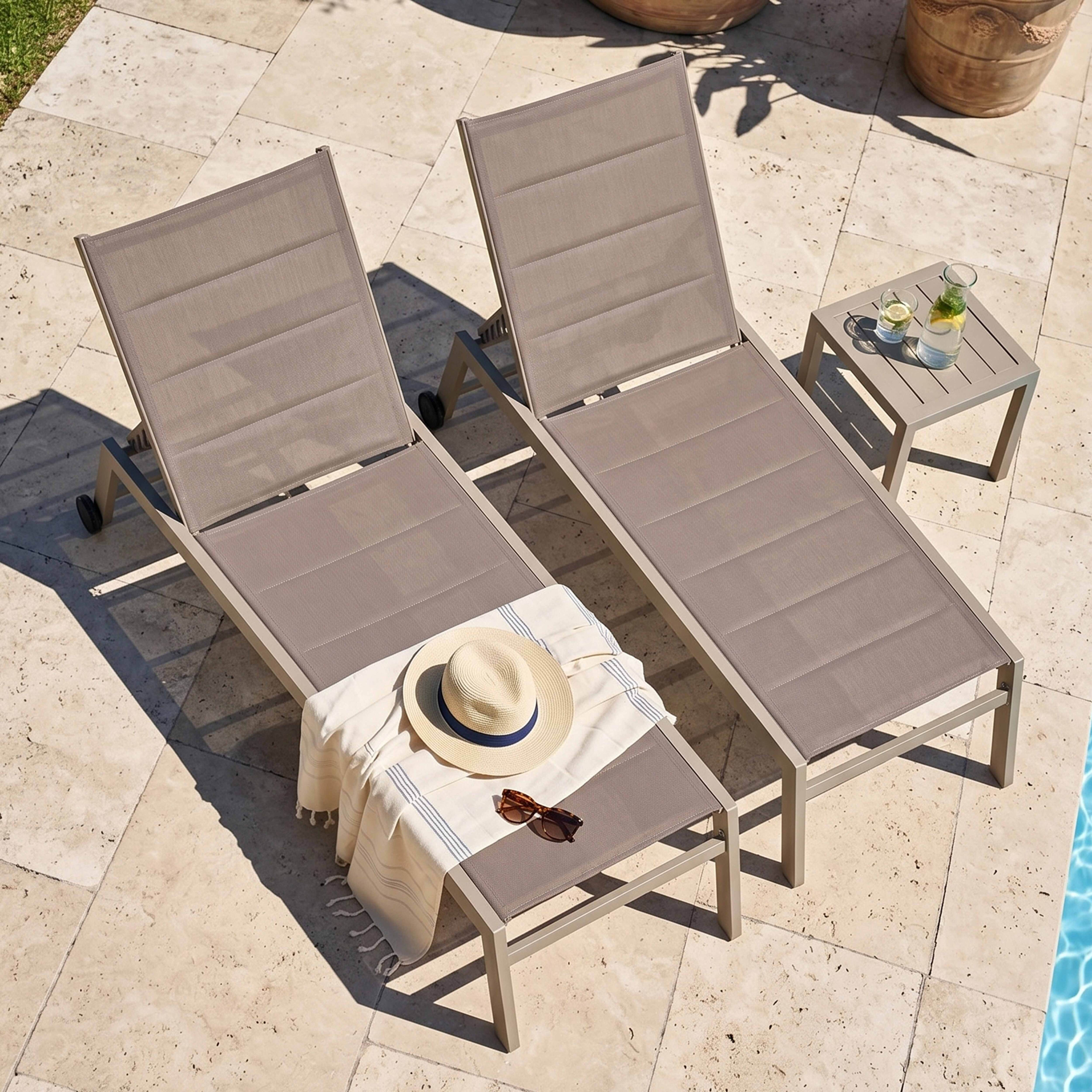 Zwei Liegestühle am Pool mit Hut, Sonnenbrille, Handtuch, Tisch mit Getränken.
