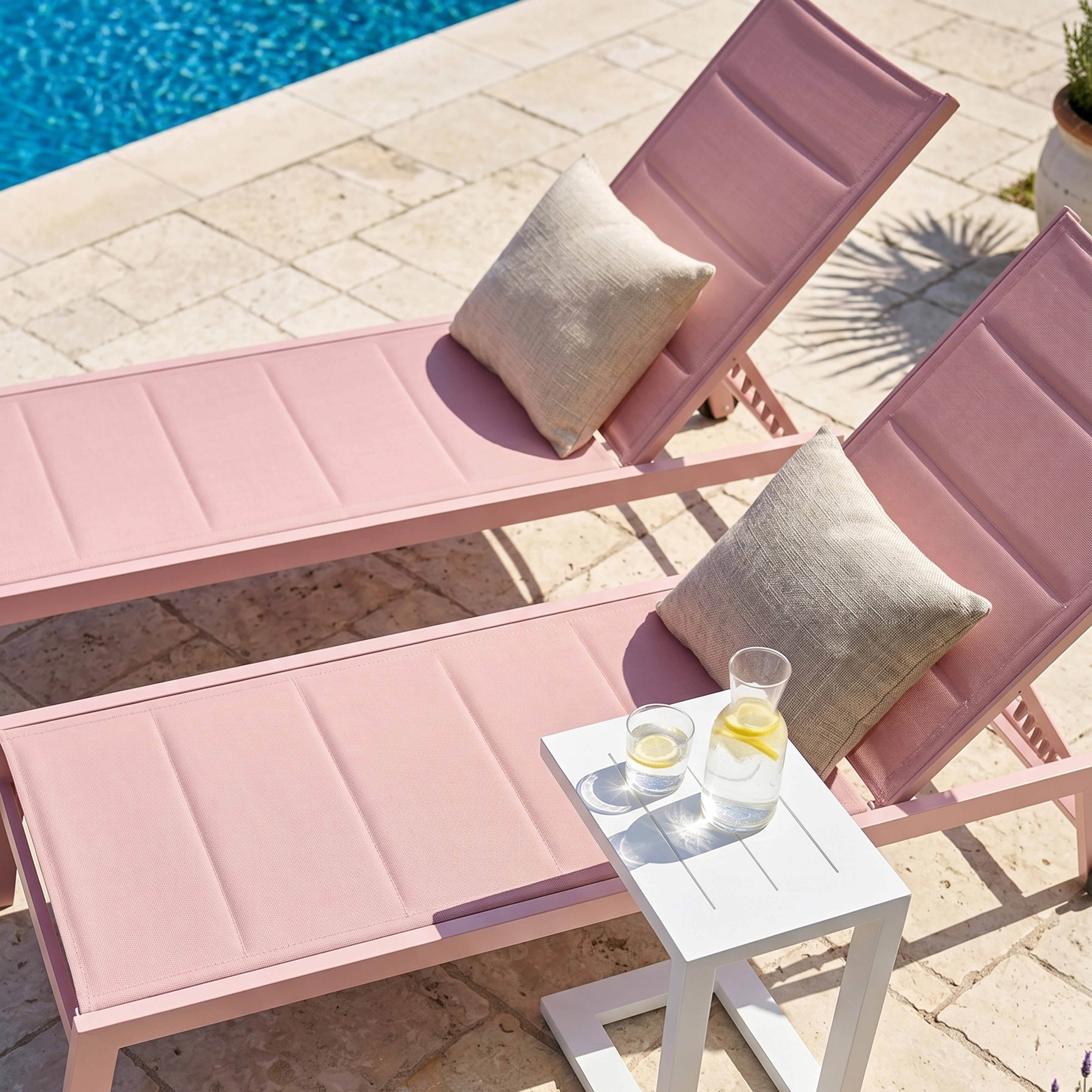 Zwei rosafarbene Liegestühle am Pool, mit einem Beistelltisch, auf dem Getränke stehen.