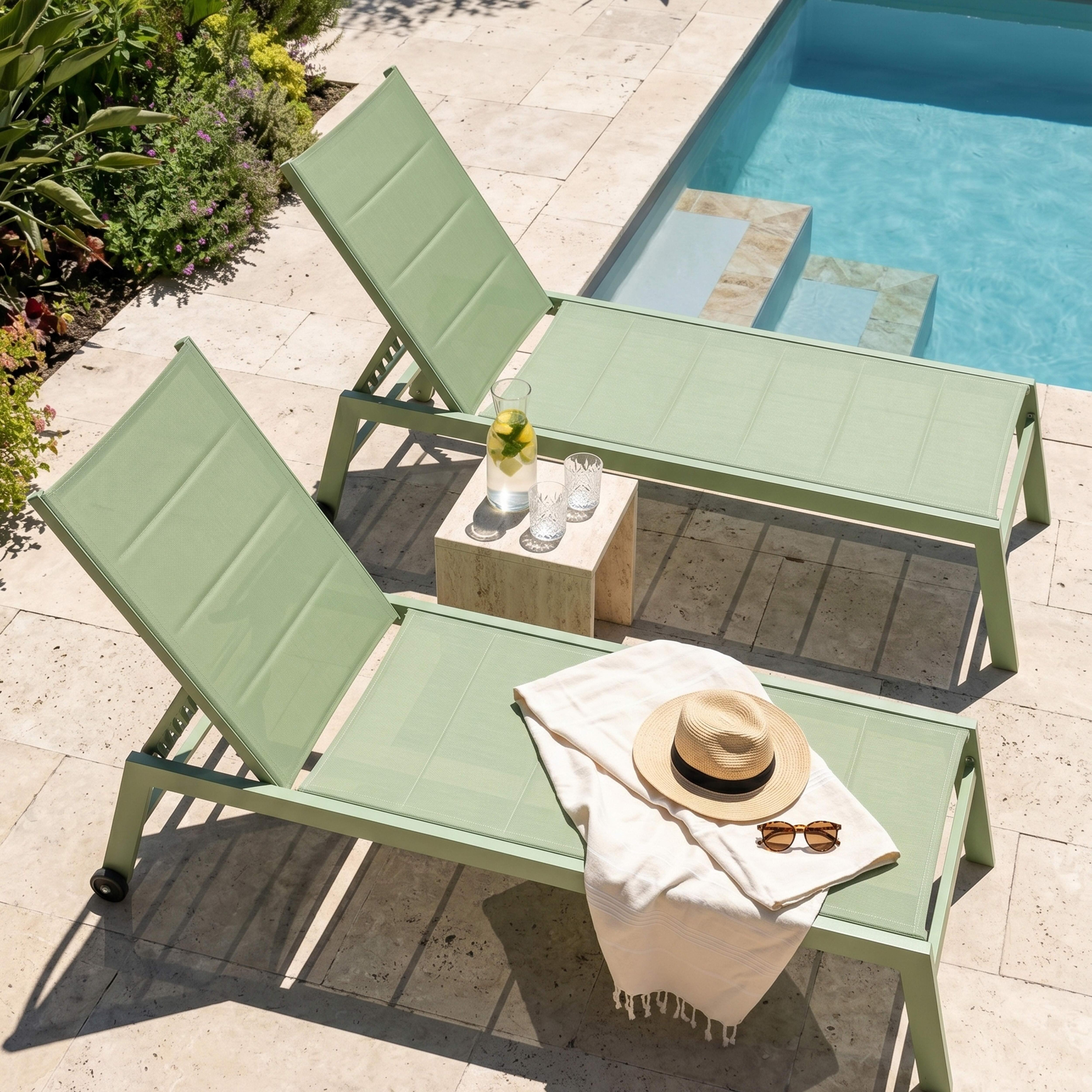 Zwei grüne Liegestühle am Pool mit Wasser, Zitrone und Gläsern.