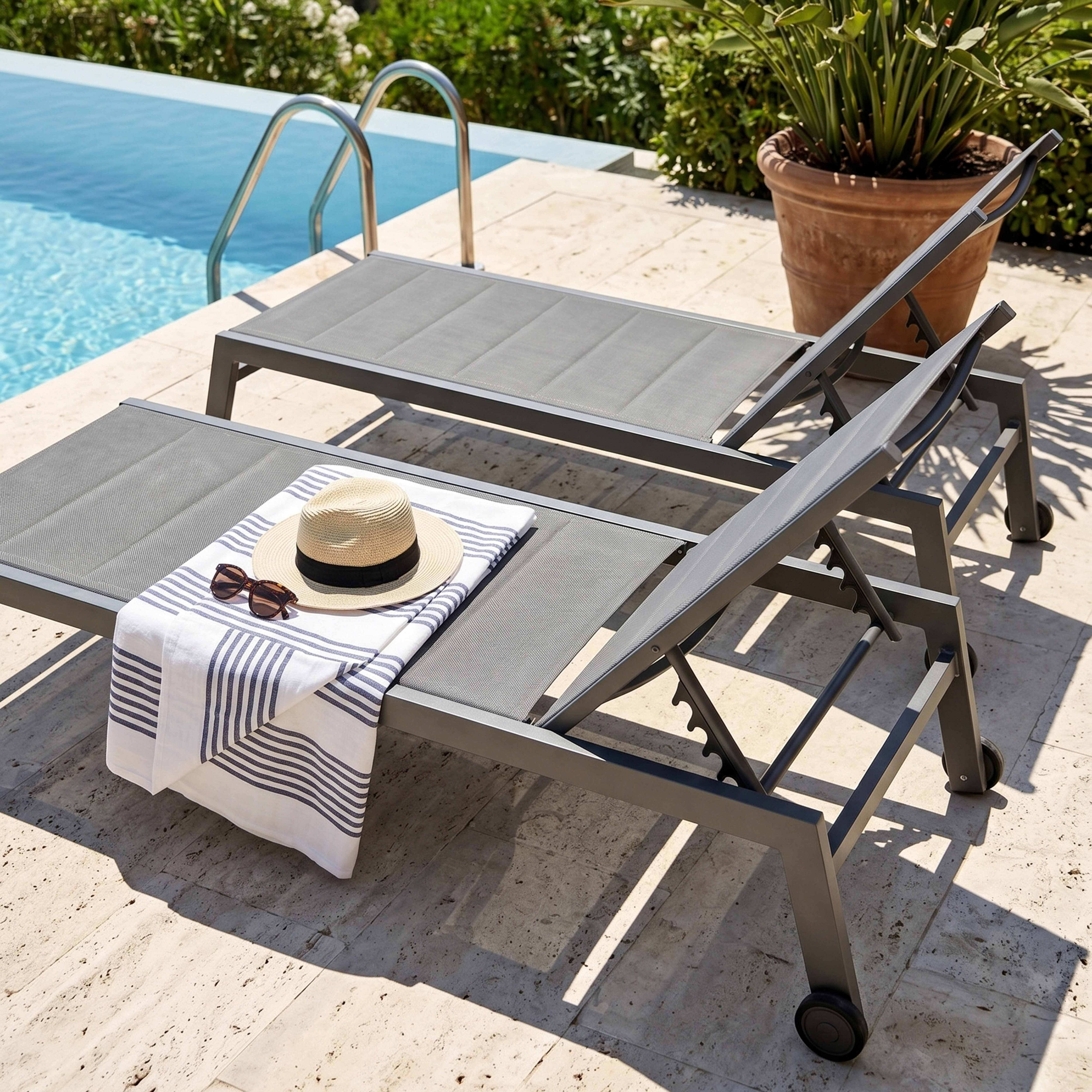 Zwei graue Liegestühle am Pool mit Handtuch, Sonnenbrille und Hut.