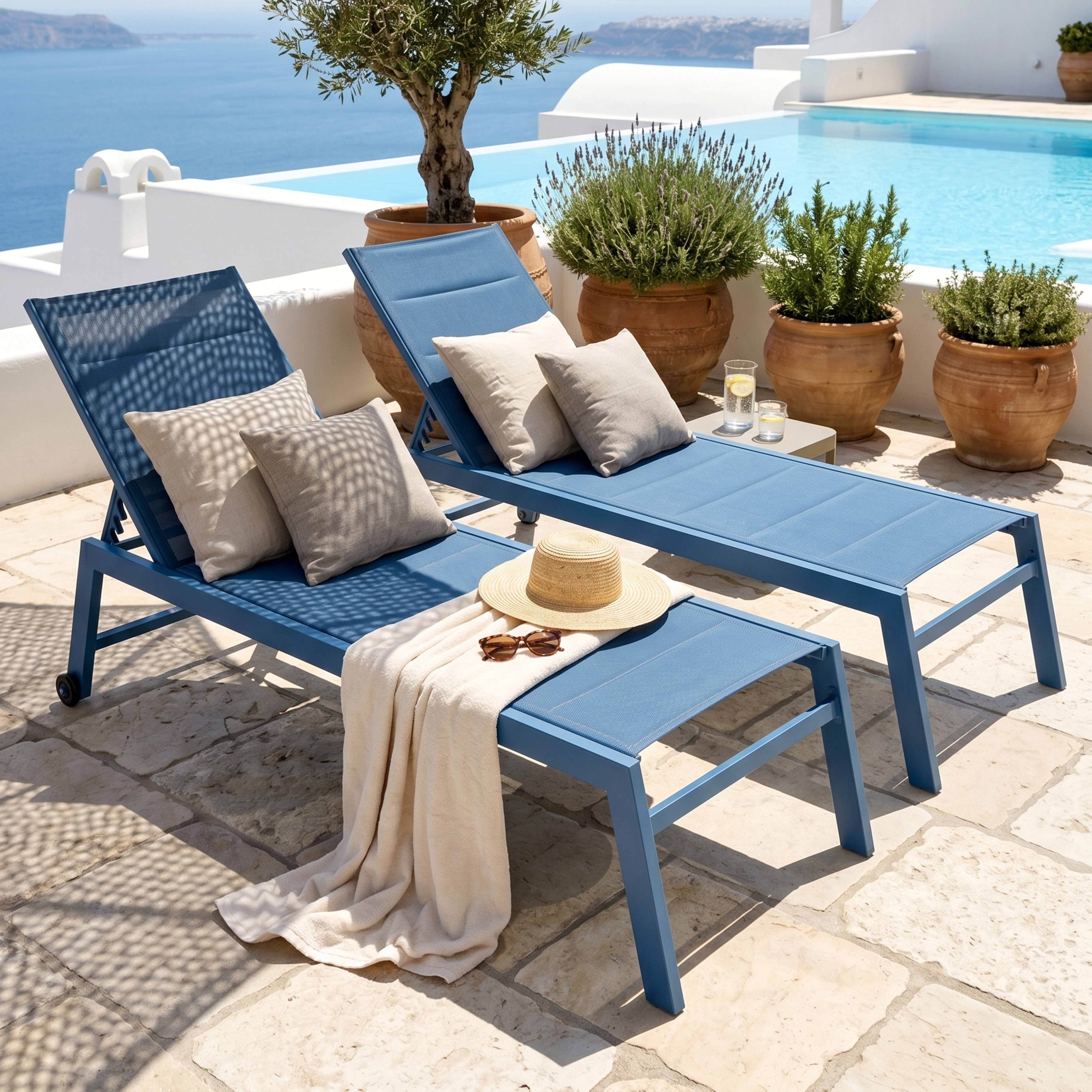 Zwei blaue Liegestühle mit Kissen am Pool mit Blick aufs Meer.