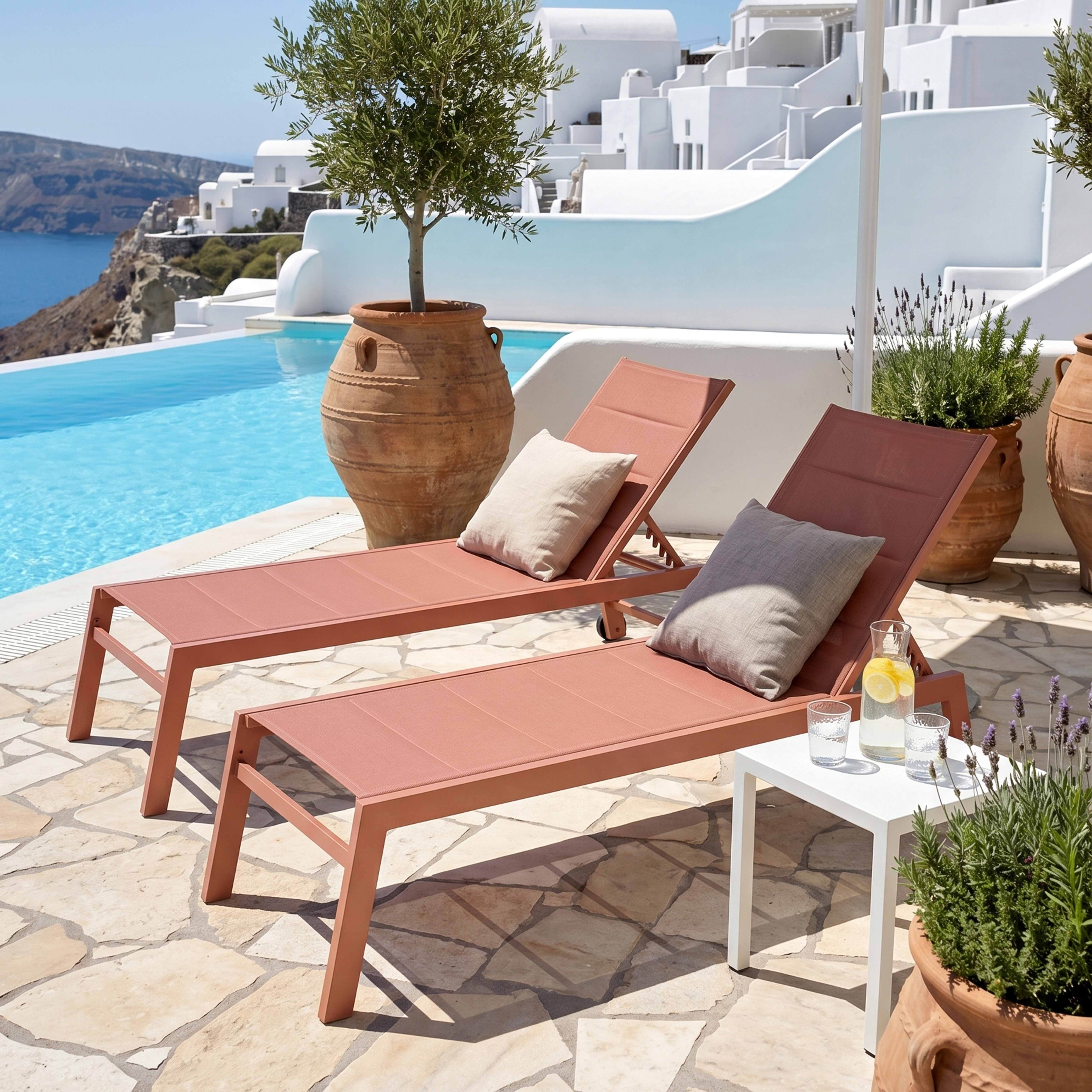 Zwei Korallenrote Liegestühle am Pool mit Blick auf das Meer und weiße Gebäude.
