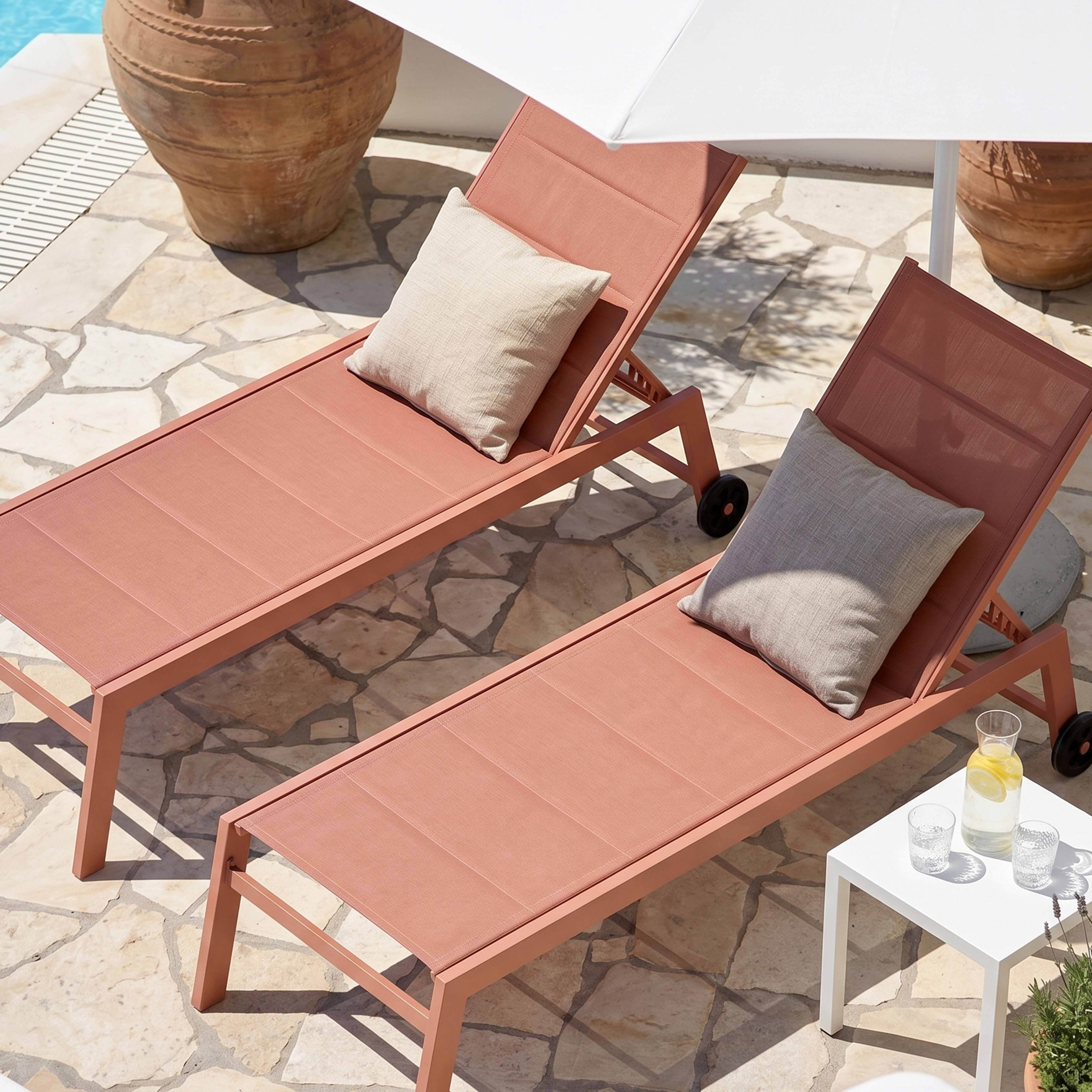 Zwei Korallenfarbene Liegestühle mit Kissen und Sonnenschirm am Pool.