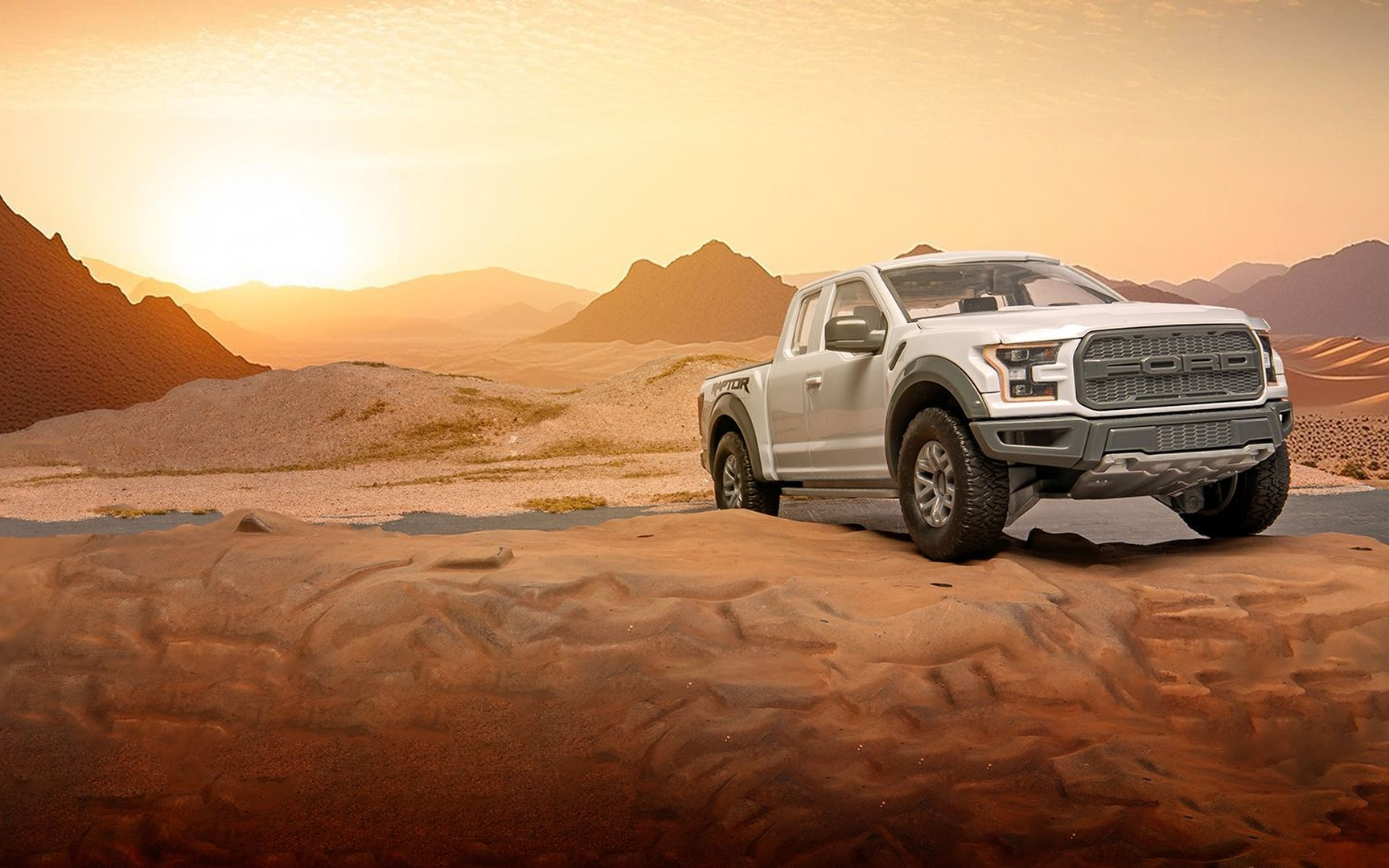 Biały pickup Ford Raptor zaparkowany na pustynnym pustkowiu o zachodzie słońca.