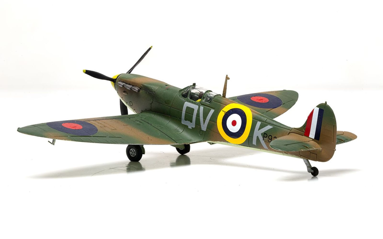 Zielono-brązowy model samolotu Spitfire z szewronami i oznaczeniami.