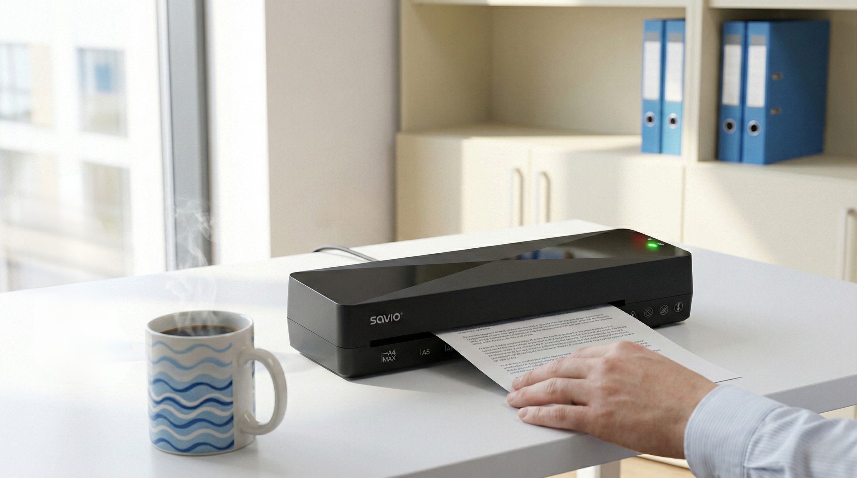 Czarna niszczarka na białym biurku przetwarzająca papier z kubkiem kawy.